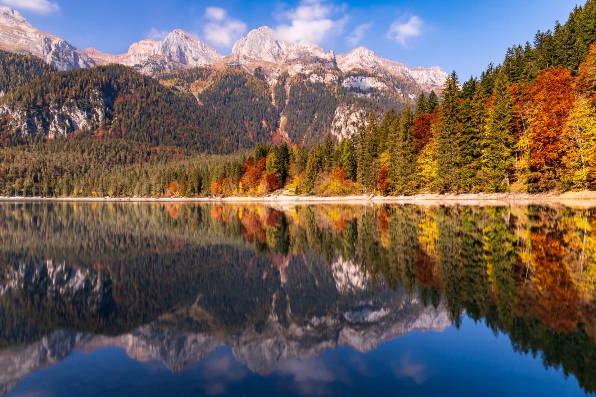 Alpine lake reflecting rugged mountains and autumn foliage under a blue sky