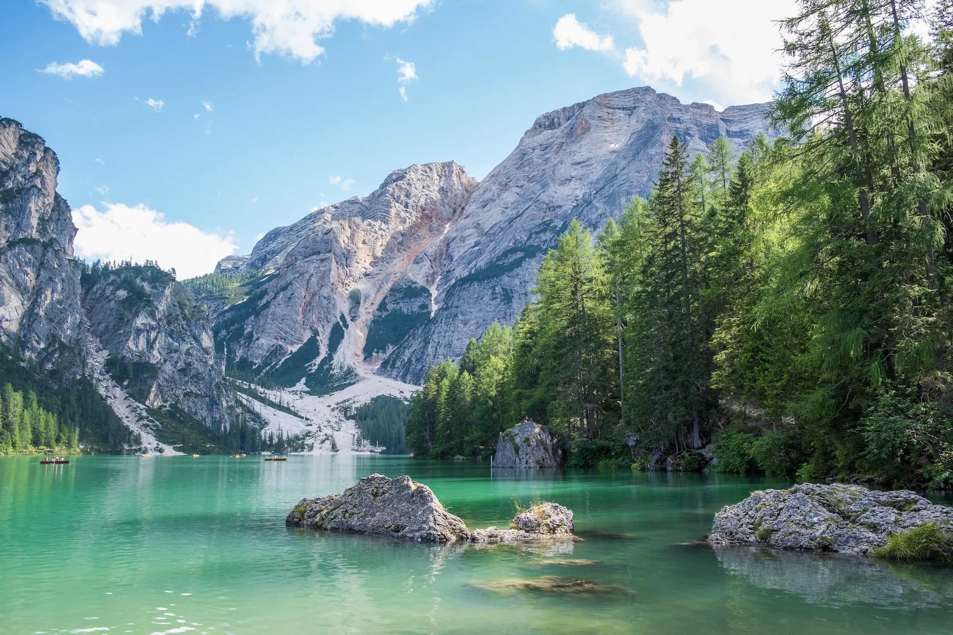 Lago di Braies with emerald water, rocky mountains, and rowboats on a sunny day.