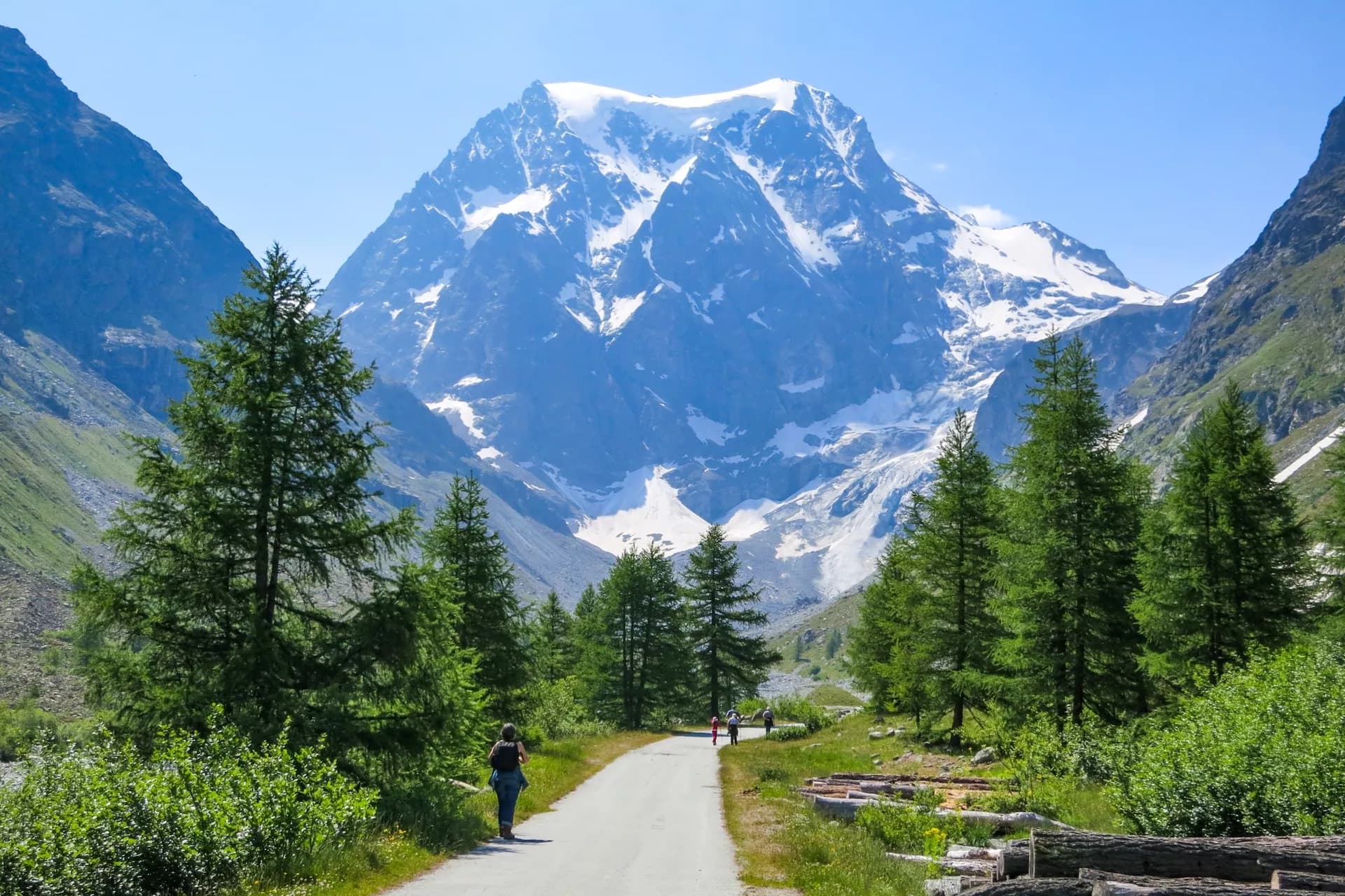 Hikers on path toward Mont Collon with snow-capped alpine peaks near Arolla.