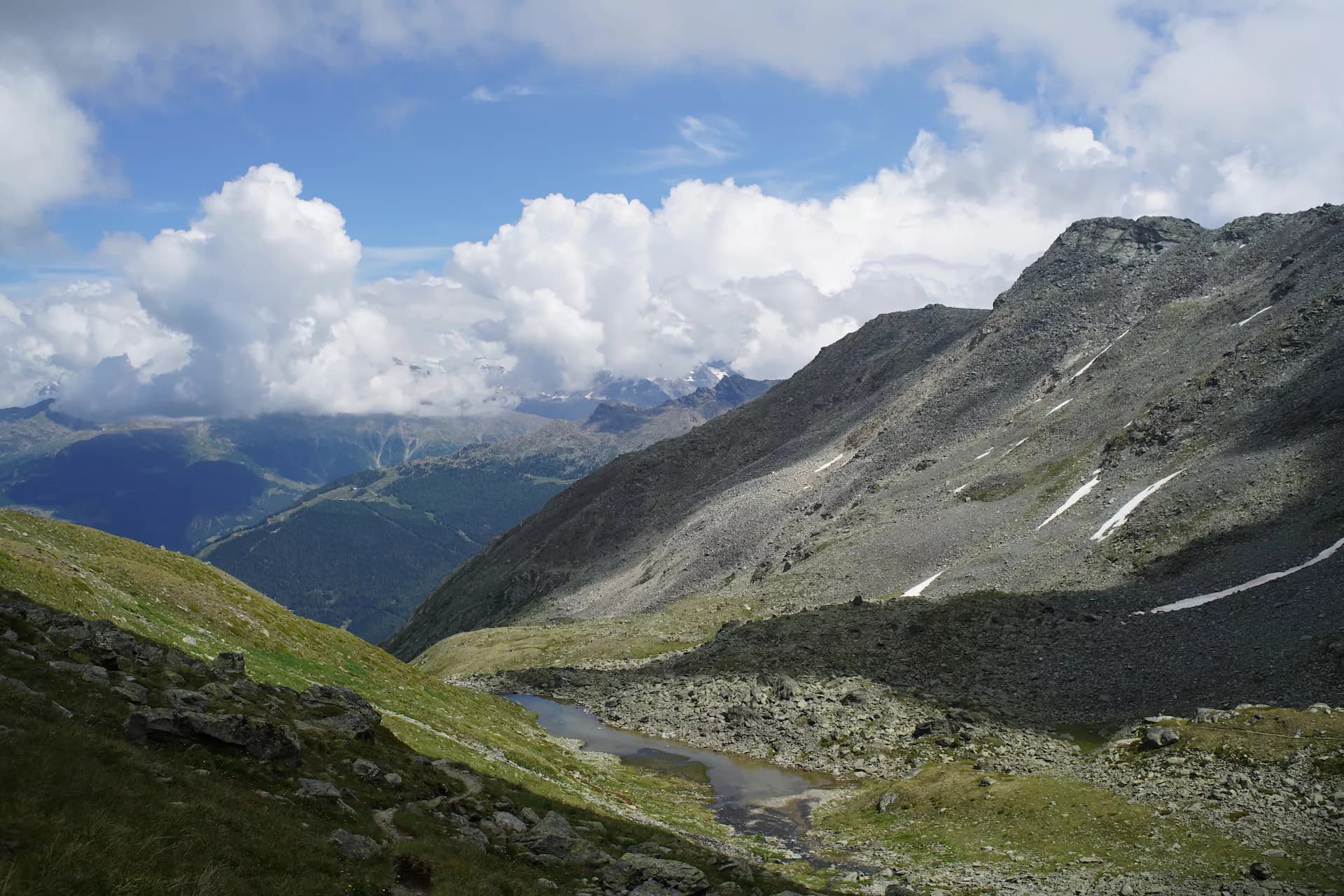 Alpine tarn nestled between rocky slopes under a cloudy blue sky near Augstbordpass.