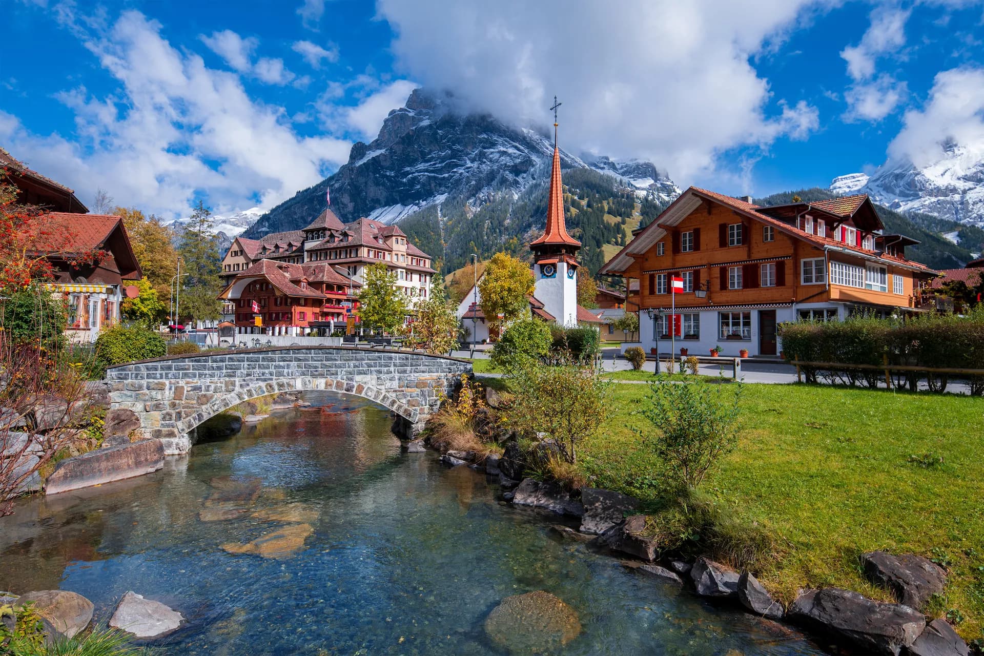 Alpine village Kandersteg with stone bridge over stream and snow-capped Dundenhorn mountain.