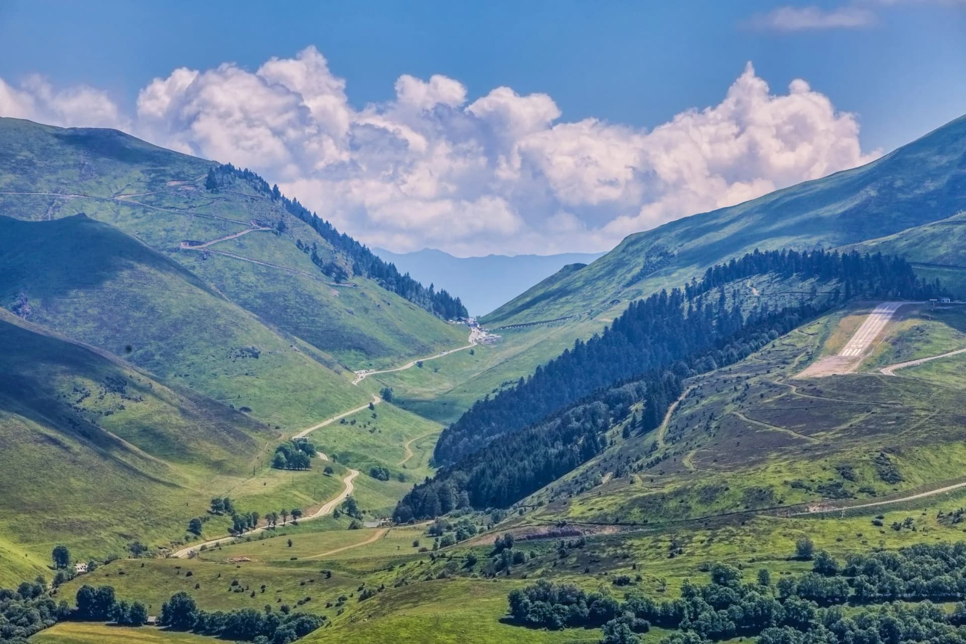 Winding road through green mountain valley with an airstrip on the slope, Col de Peyresourde.