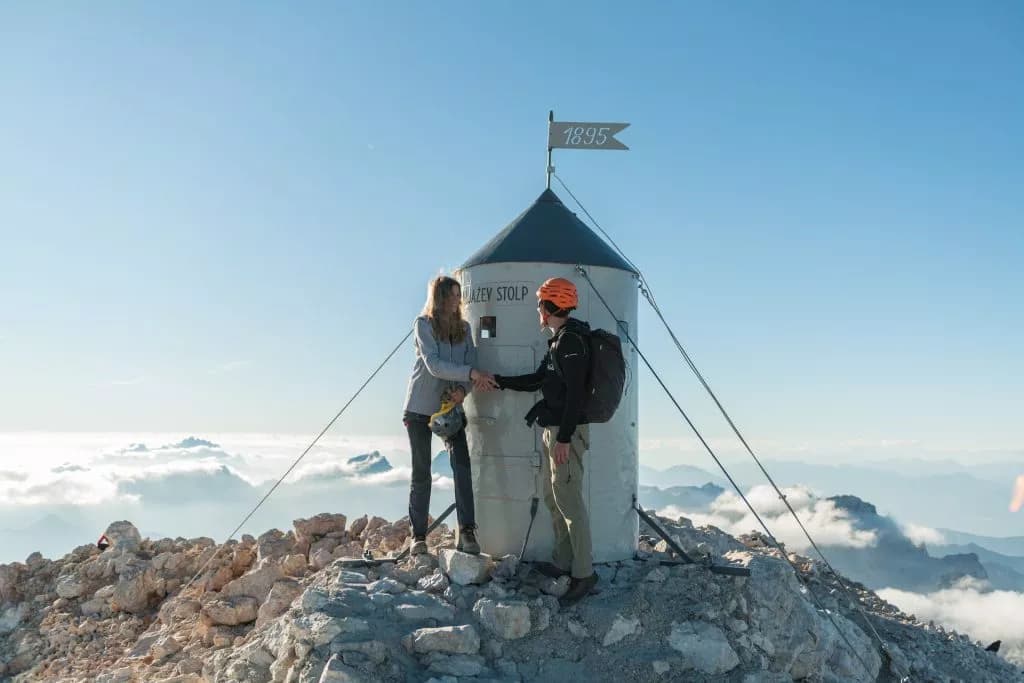 Hikers shaking hands at Aljažev Stolp on Mount Triglav above the clouds.