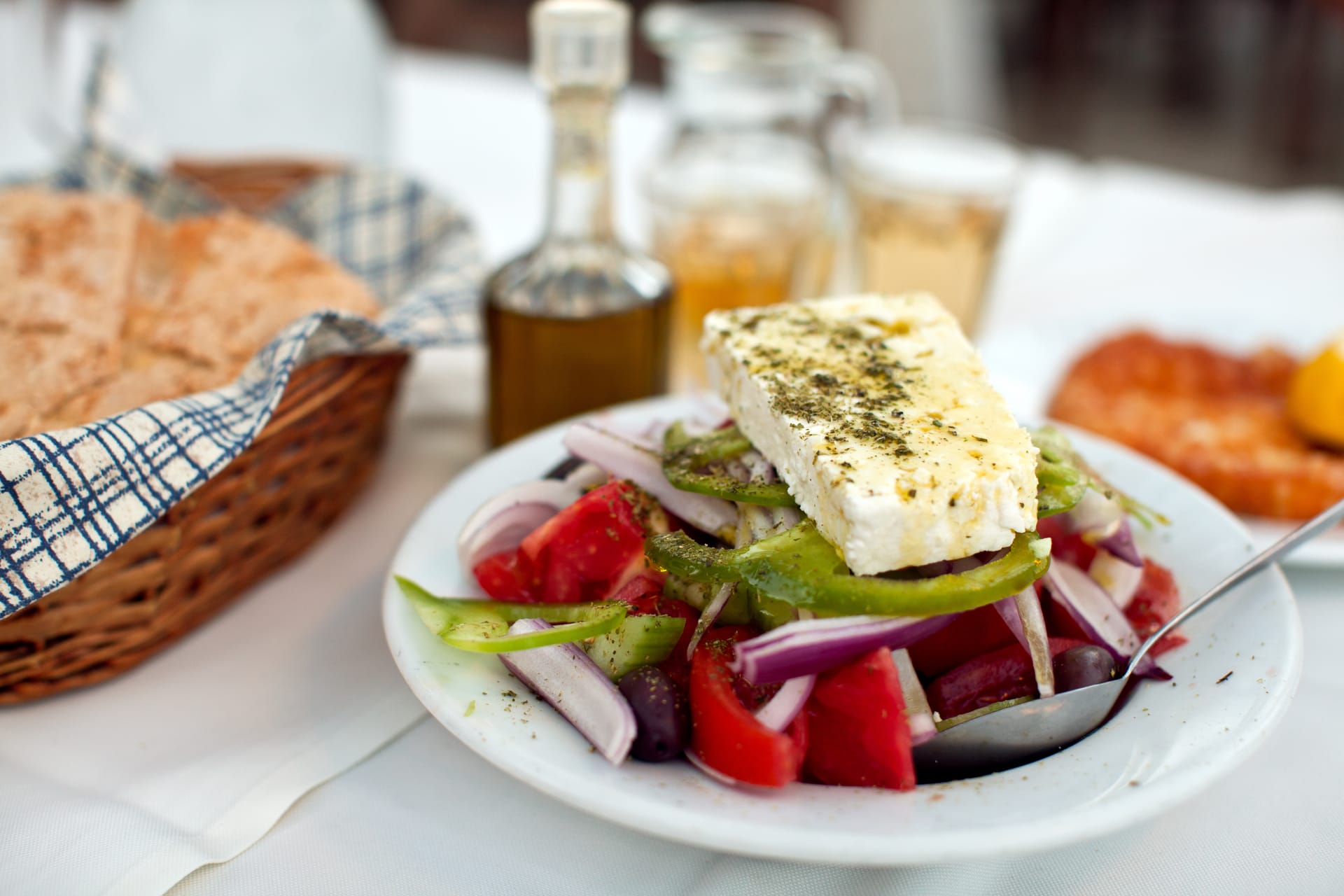 Greek salad with feta cheese, tomatoes, and olives served outdoors with bread and drinks.