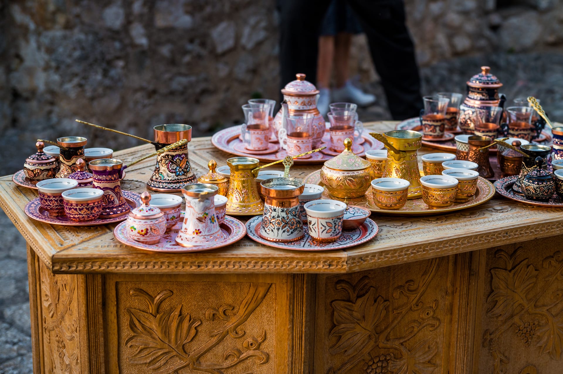 Ornate copper and ceramic Bosnian coffee sets displayed on a carved wooden table.
