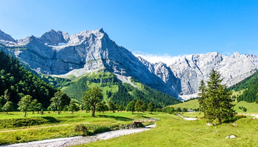 Steep rock faces and green meadows with a small bridge over a stream in the mountains