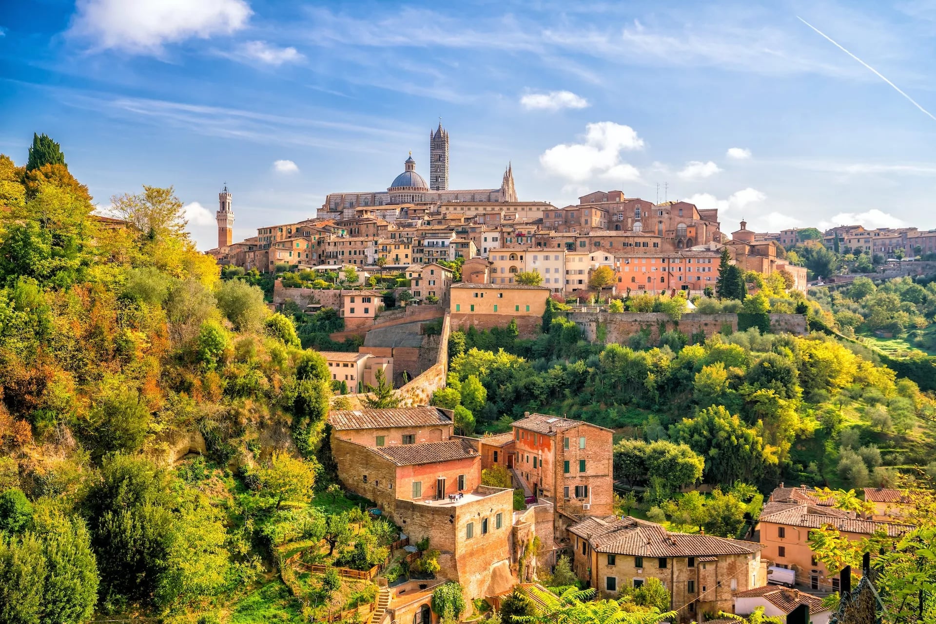 Historic hillside city of Siena with terracotta buildings and Duomo towers under a blue sky.