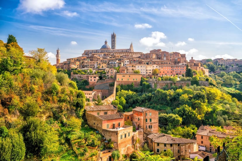 Historic hillside city of Siena with terracotta buildings and Duomo towers under a blue sky.