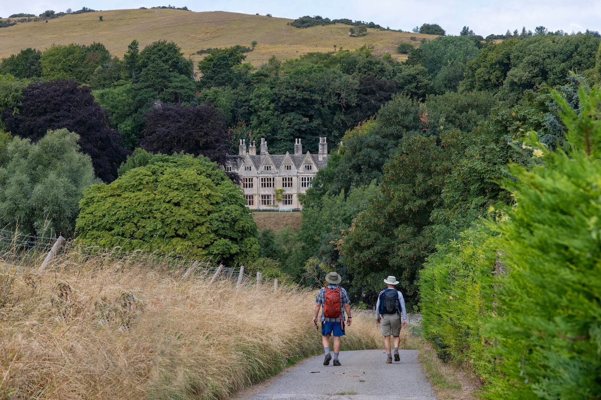 Hikers on footpath near Sudeley Castle, Cotswolds Way, with rolling hills.