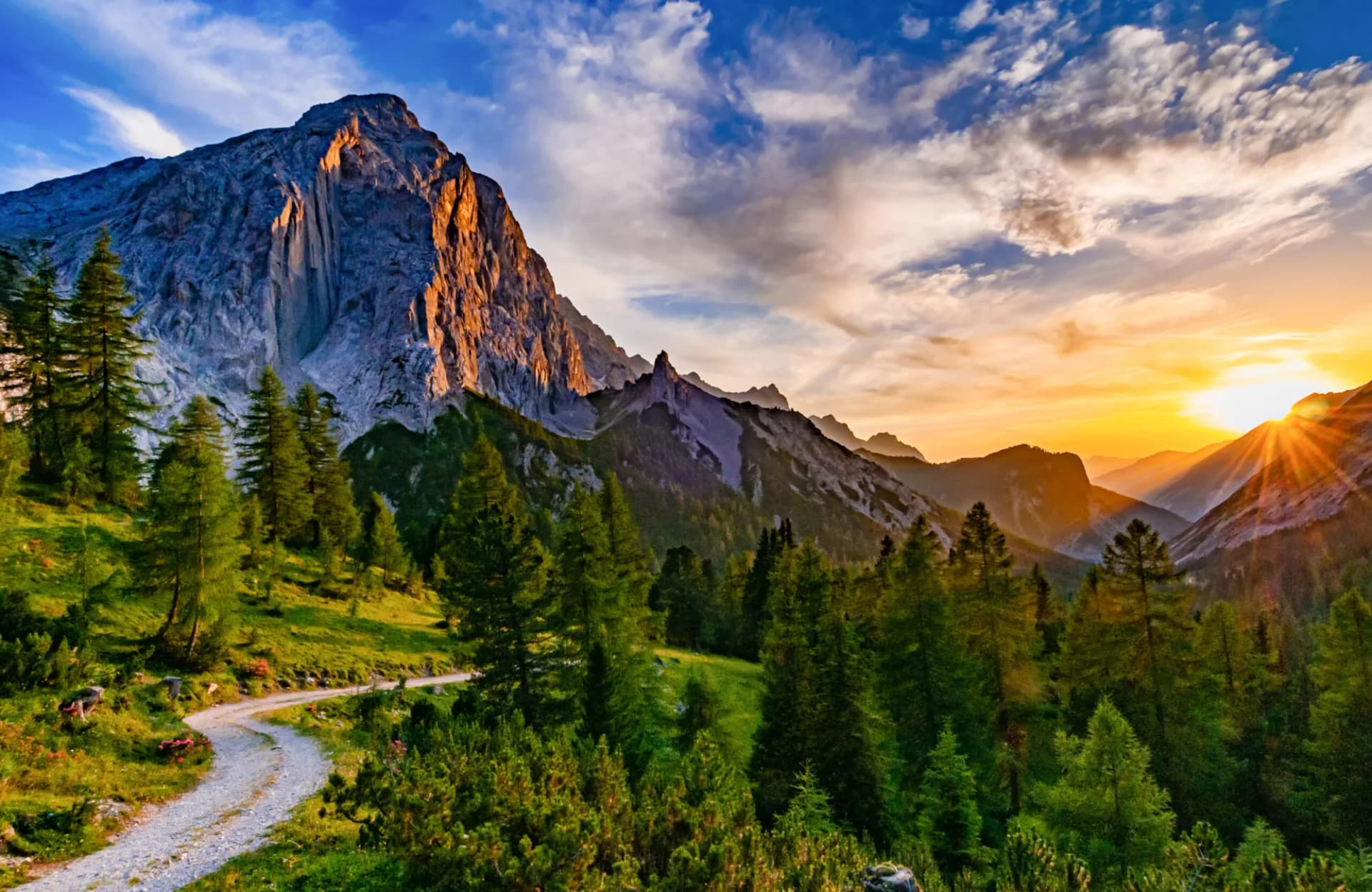 Winding dirt road near Hallerangerhaus with massive sunlit mountain at sunset