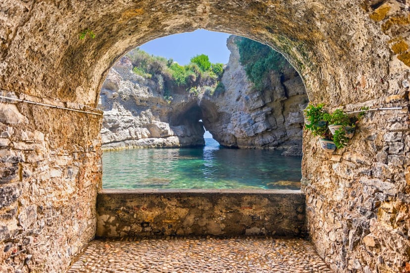 Stone archway overlooking a natural pool with a sea arch in Sorrento, Italy