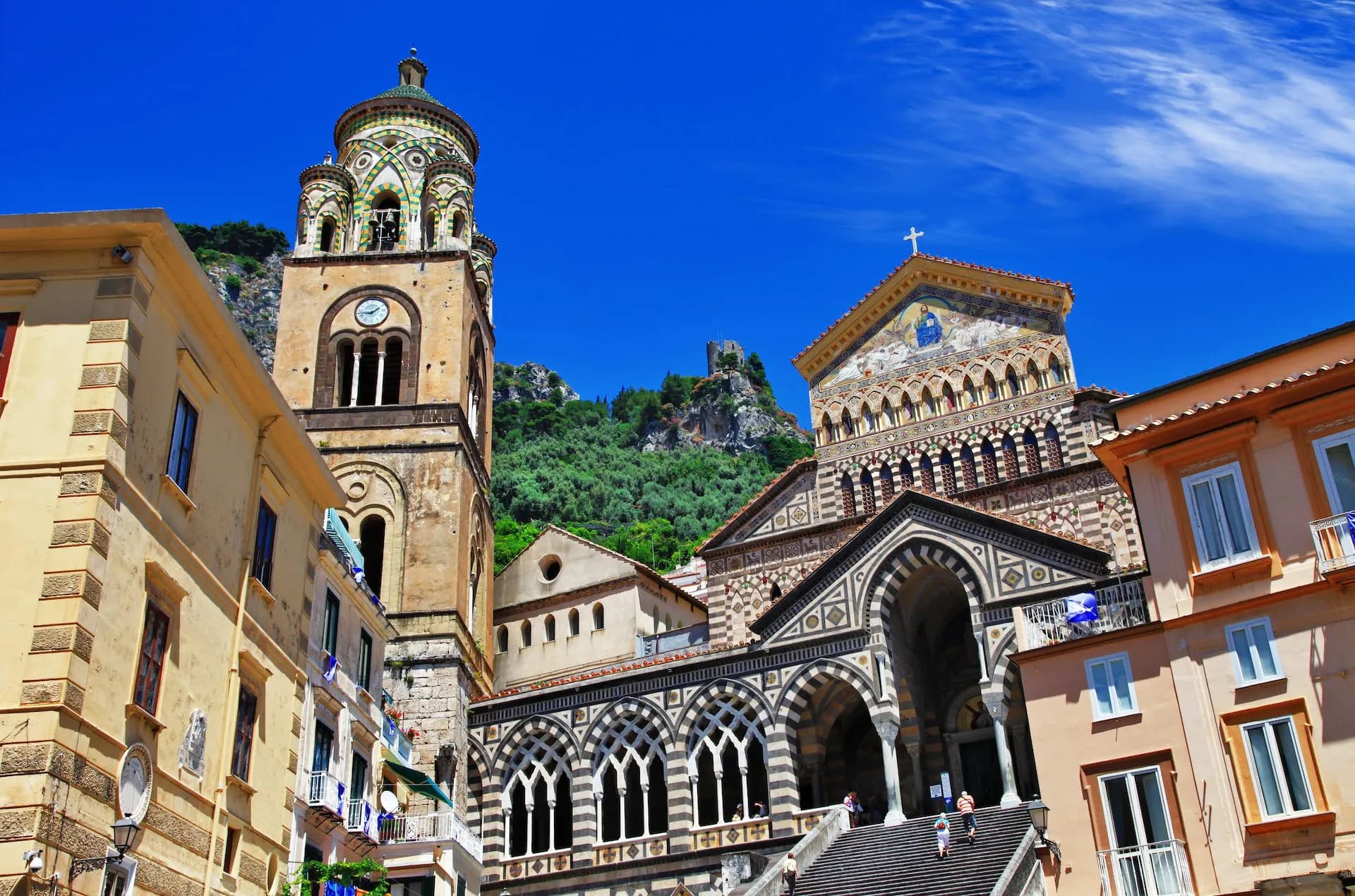 Cathedral of St. Andrea with ornate facade and bell tower against a bright blue sky in Amalfi.