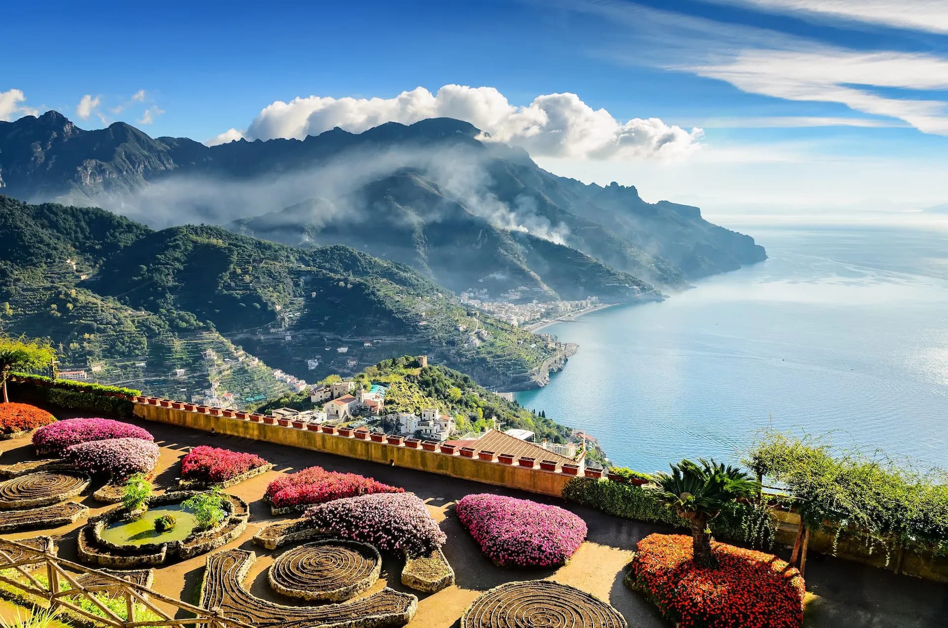 Terraced gardens with colorful flowers overlooking Ravello and the misty Amalfi Coastline.