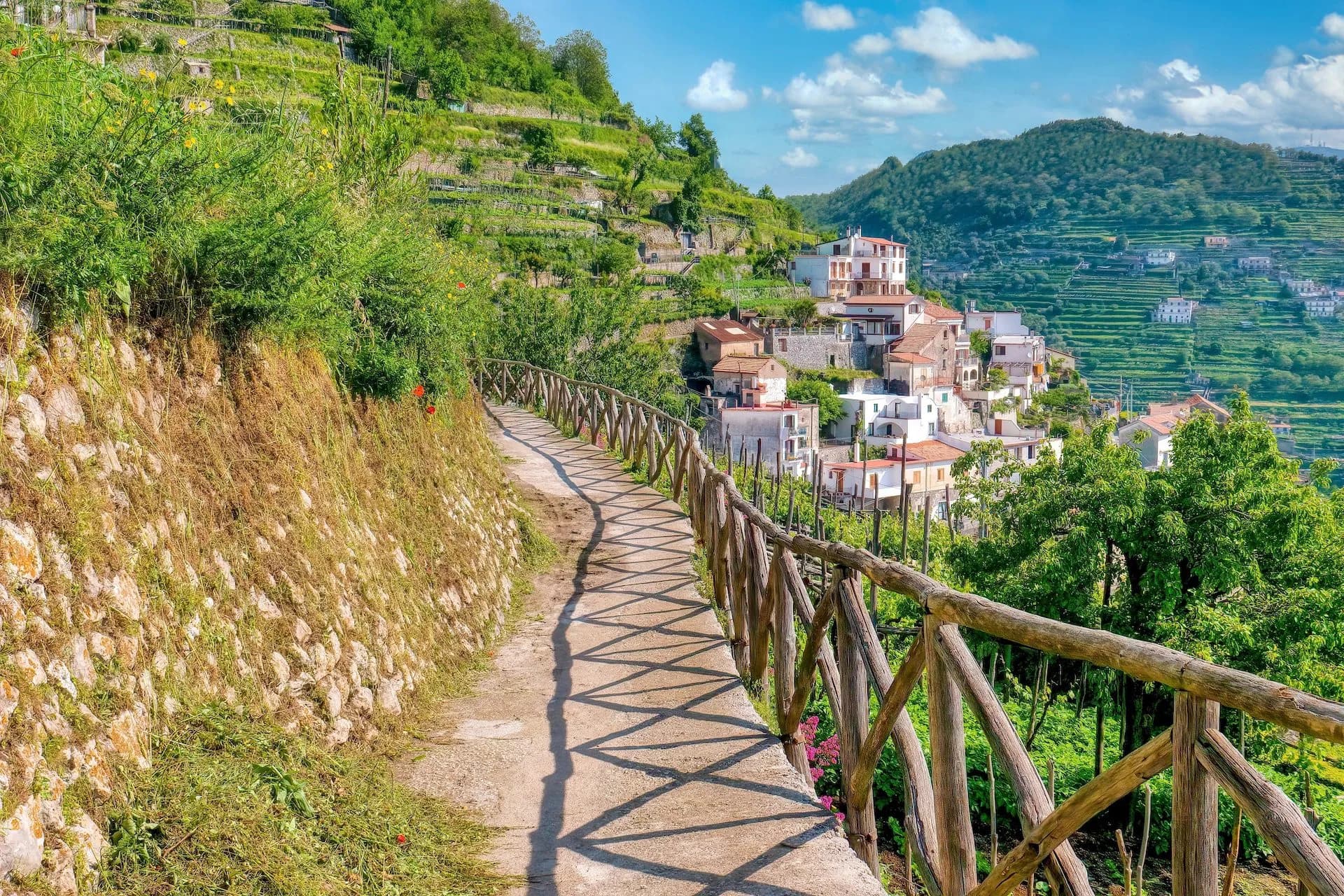Scenic footpath with wooden railing near terraced hillsides and white houses in Valle delle Ferriere.
