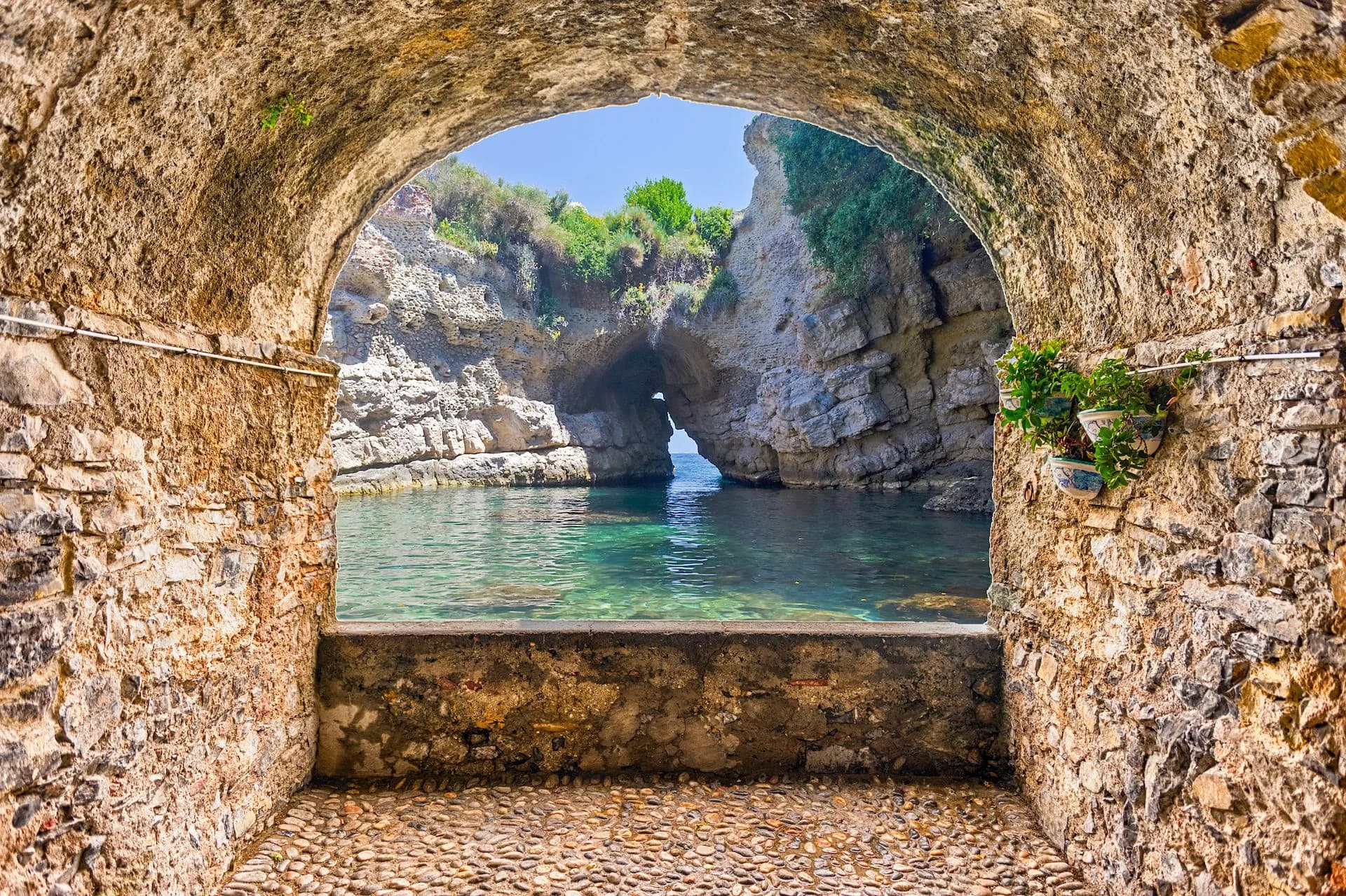 Stone archway overlooking a natural pool with rock formations and sea cave in Sorrento.