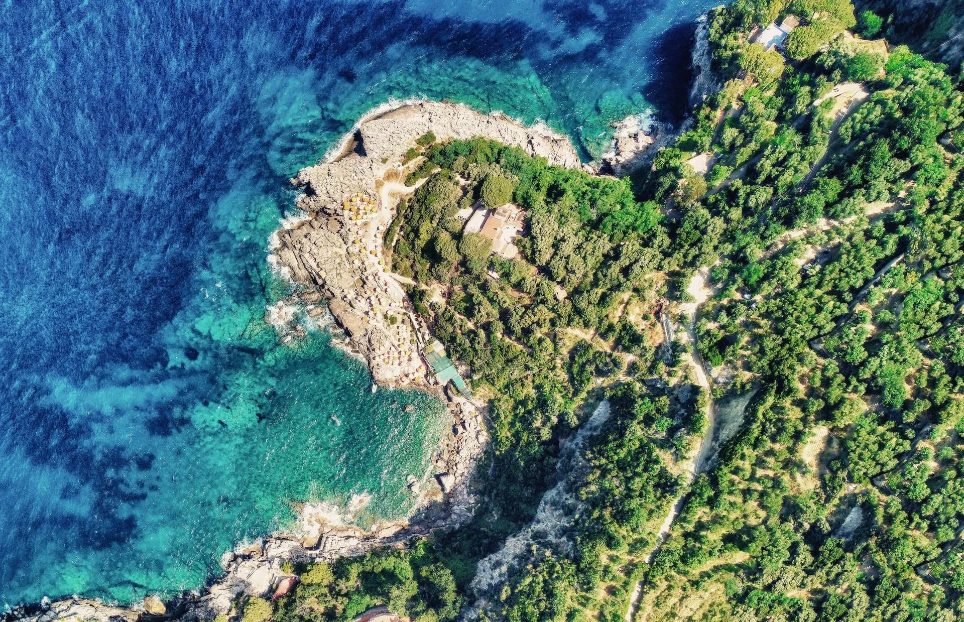 Aerial view of Punta Campanella coastline with turquoise sea, rocky shore, and dense green vegetation.