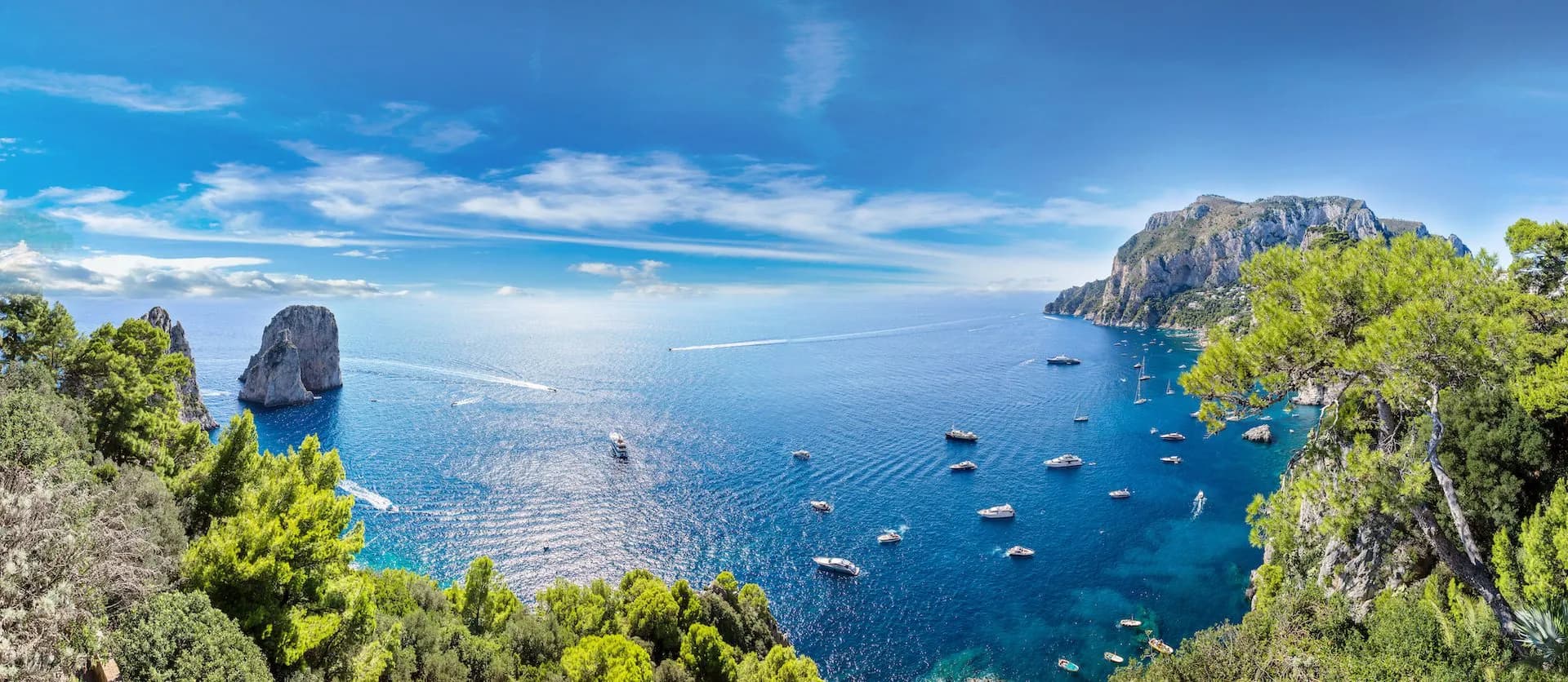 Boats on blue sea near rocky cliffs and green foliage, Capri Island, Italy.