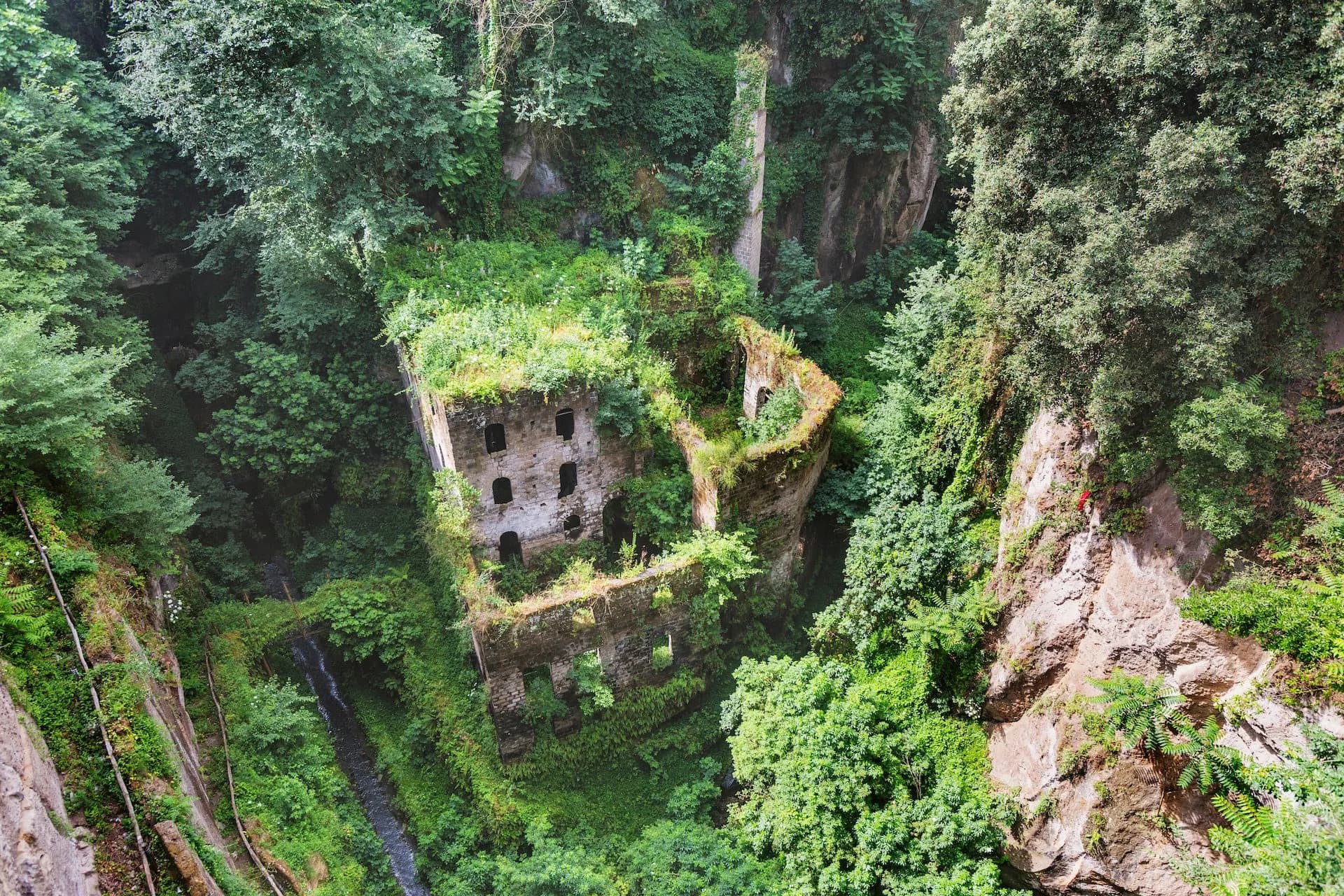 Ruins of Valle dei Mulini overgrown with lush greenery in a deep ravine near Sorrento.