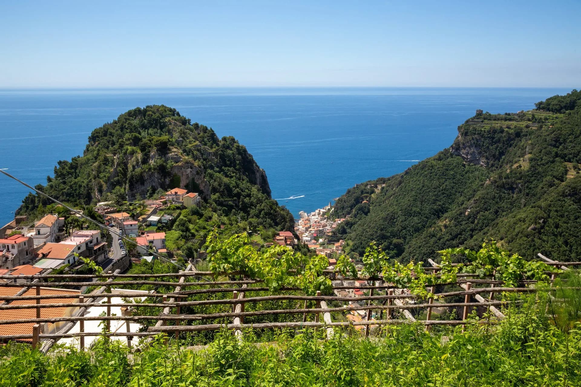 View of Pontone village nestled between green hills overlooking the blue sea from a vineyard.