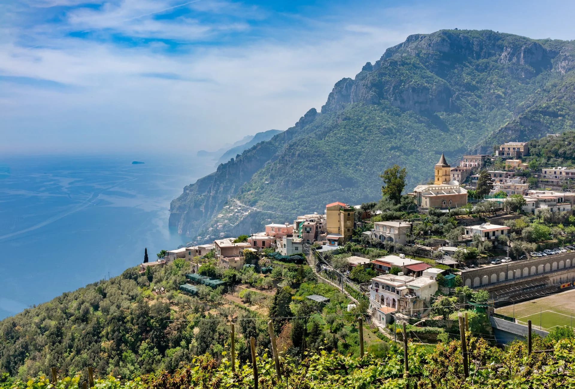 Vineyard overlooking Montepertuso village houses, steep green mountains, and the blue sea.
