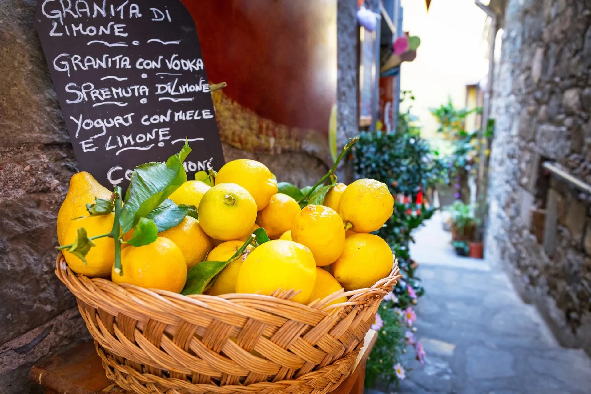 Basket of fresh lemons next to a chalkboard menu in a narrow, stone-walled alley in Cinque Terre.