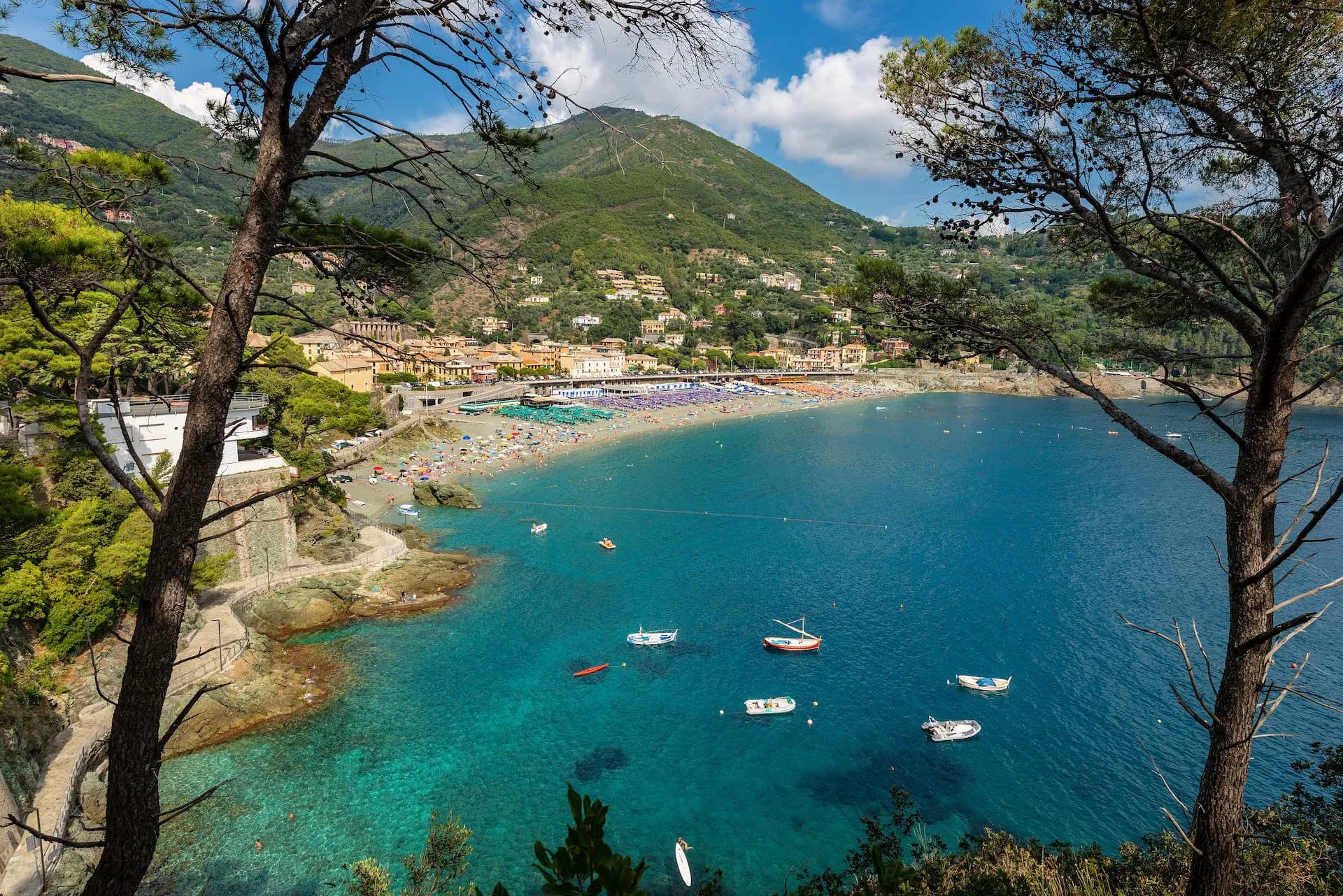 Boats on turquoise bay near crowded beach backed by green hills in Bonassola