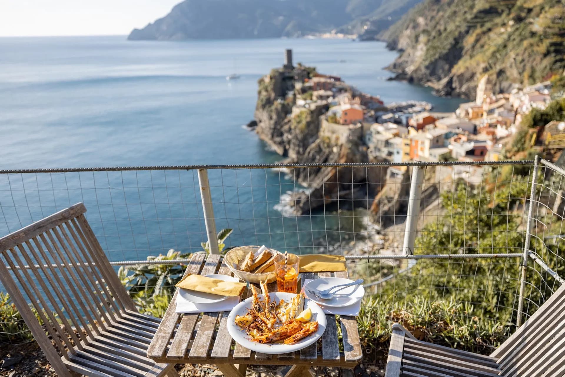 Outdoor seafood meal overlooking Vernazza village and the Mediterranean Sea coastline.