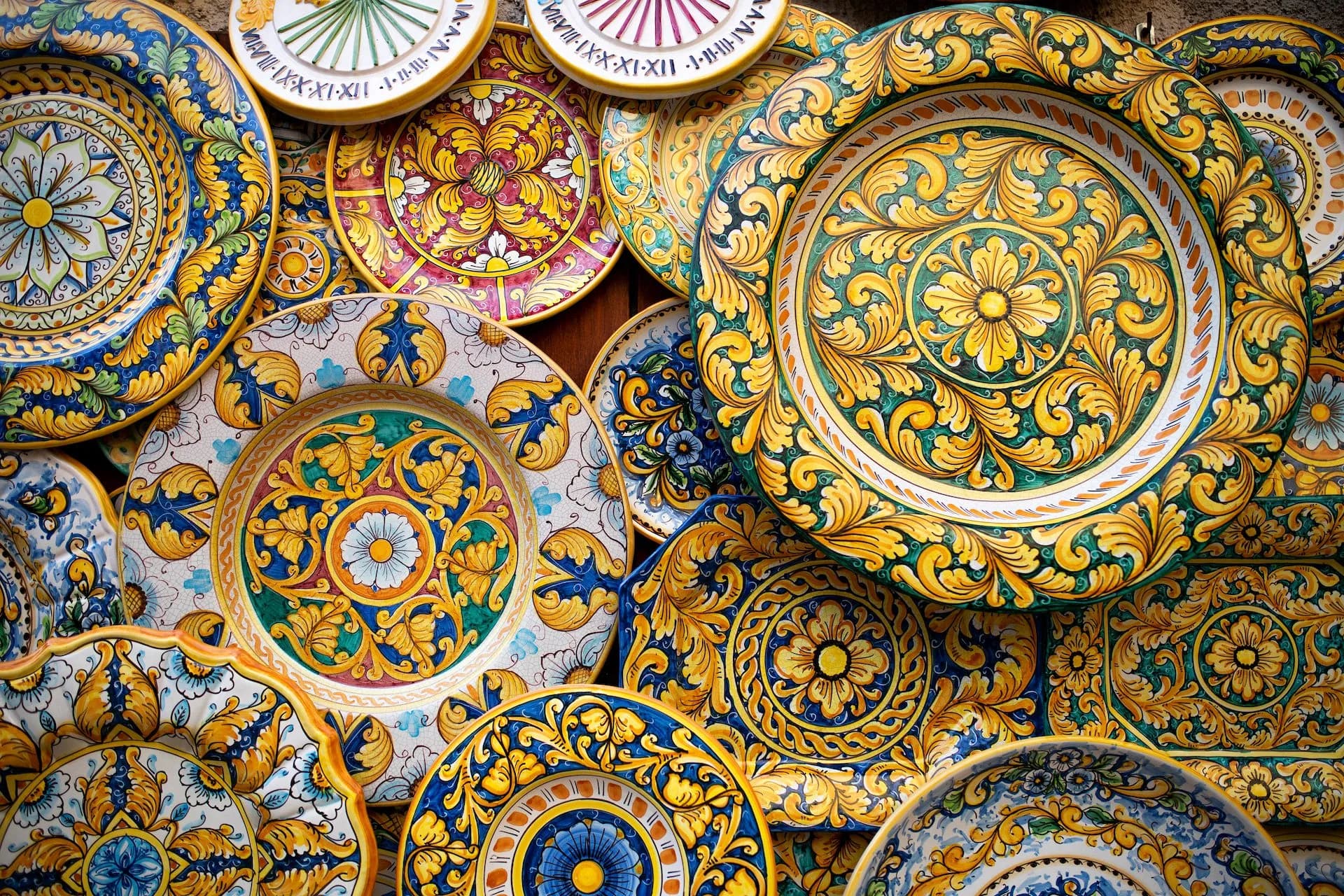 Colorful hand-painted ceramic plates with yellow, blue, and green floral patterns, Sicilian handicraft.