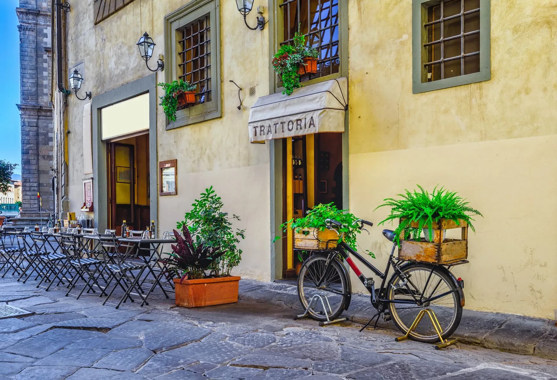 Trattoria entrance with outdoor seating, bicycle carrying plants, and stone pavement in Florence.