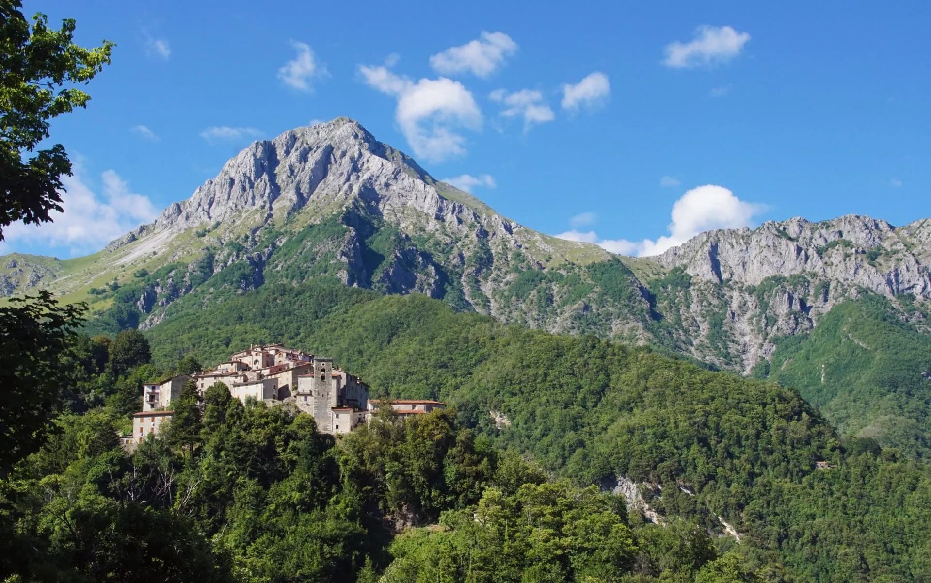 Hilltop village nestled in lush green mountains under a blue sky with white clouds.