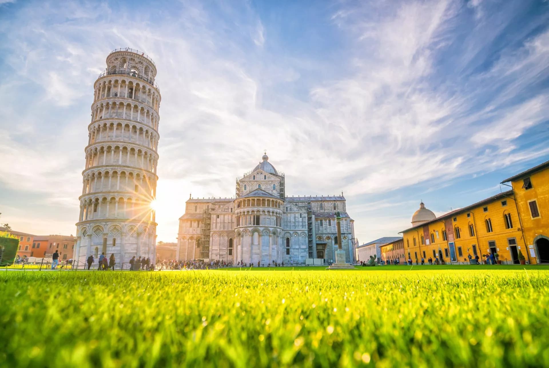 Leaning Tower of Pisa and cathedral viewed over bright green grass with sun flare