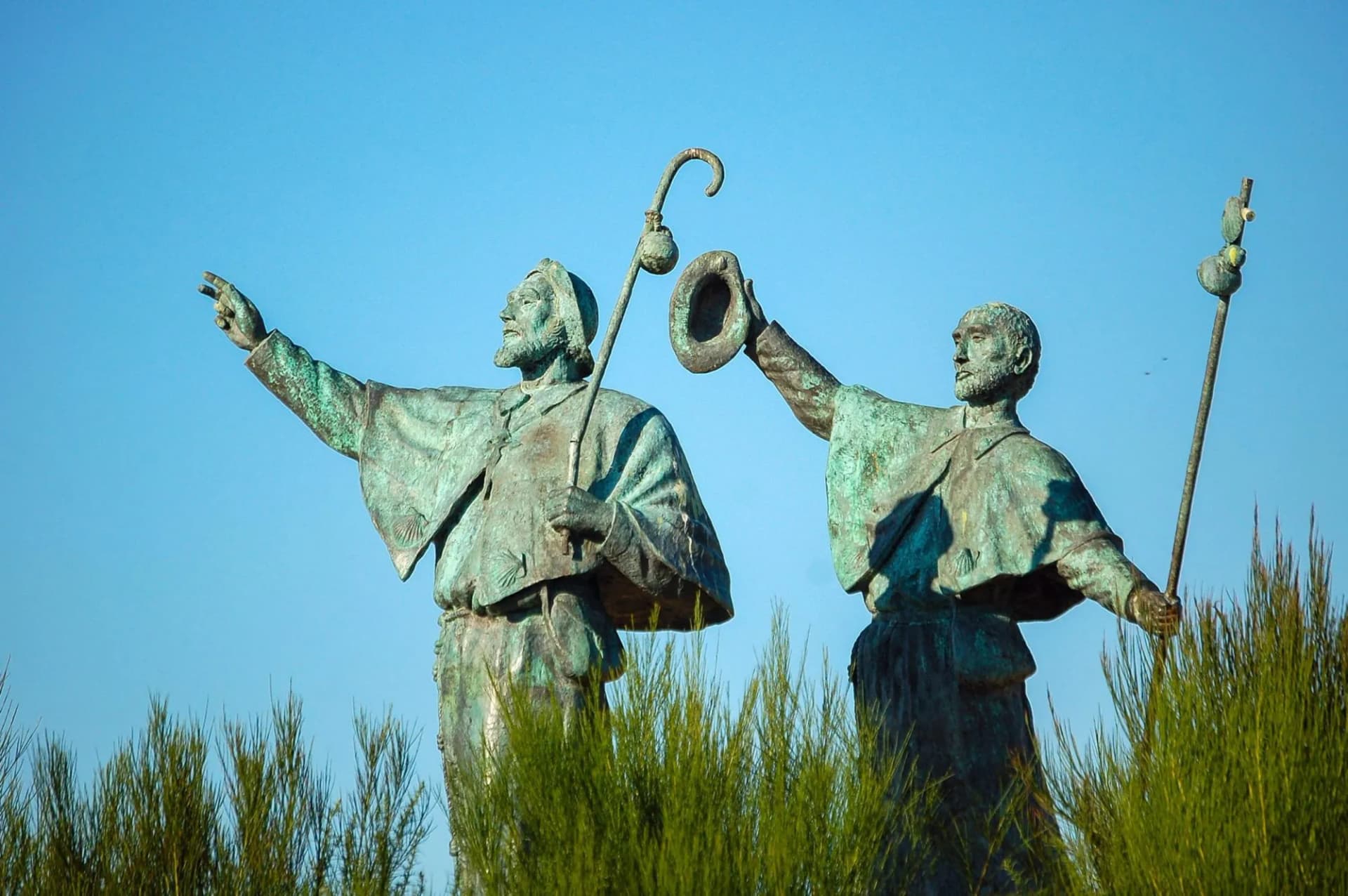 Statue of two pilgrims with staffs and hat against blue sky on the outskirts of Santiago de Compostela.