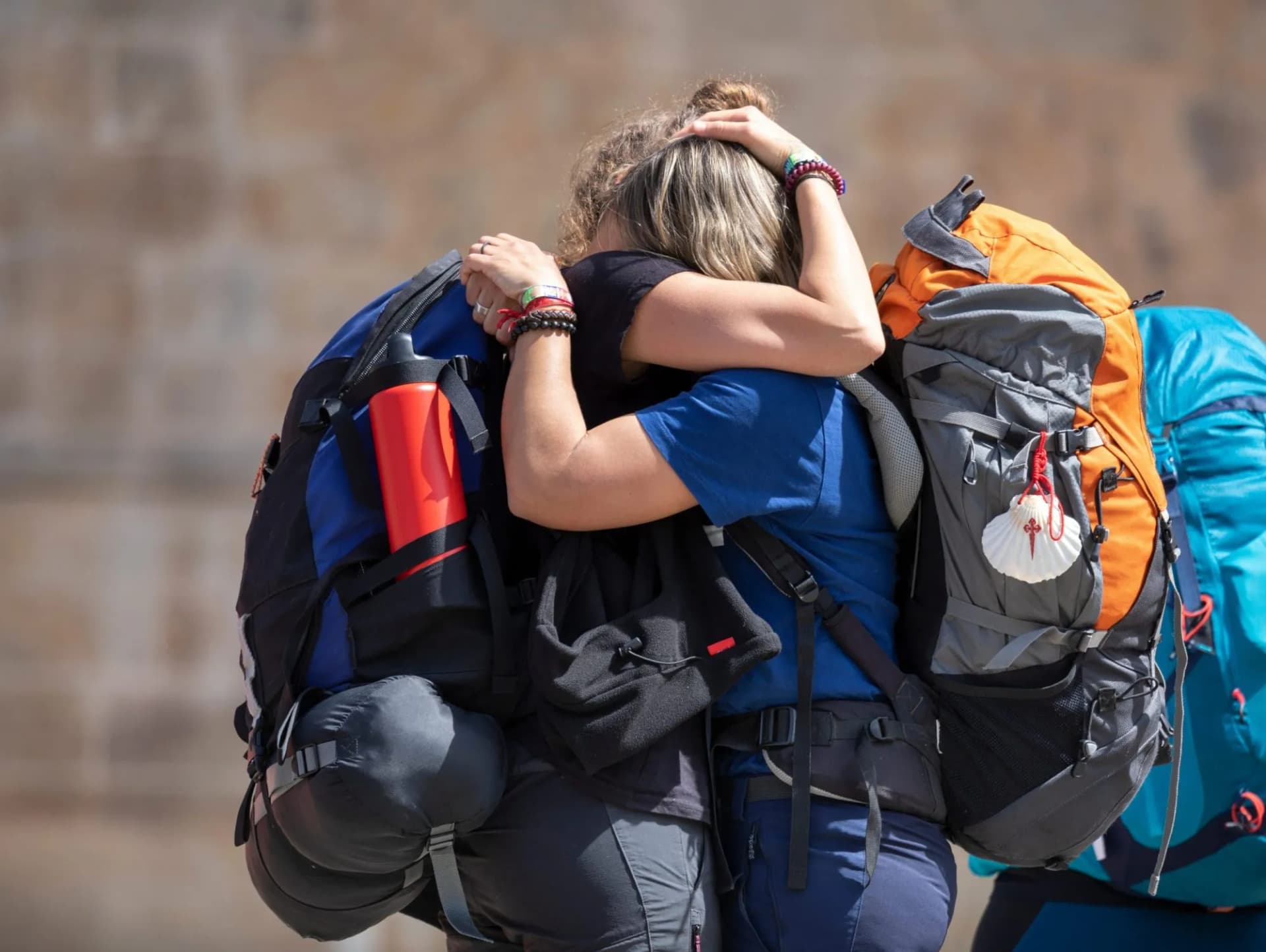 Pilgrims hugging with large backpacks, one showing a scallop shell, at Plaza del Obradoiro.