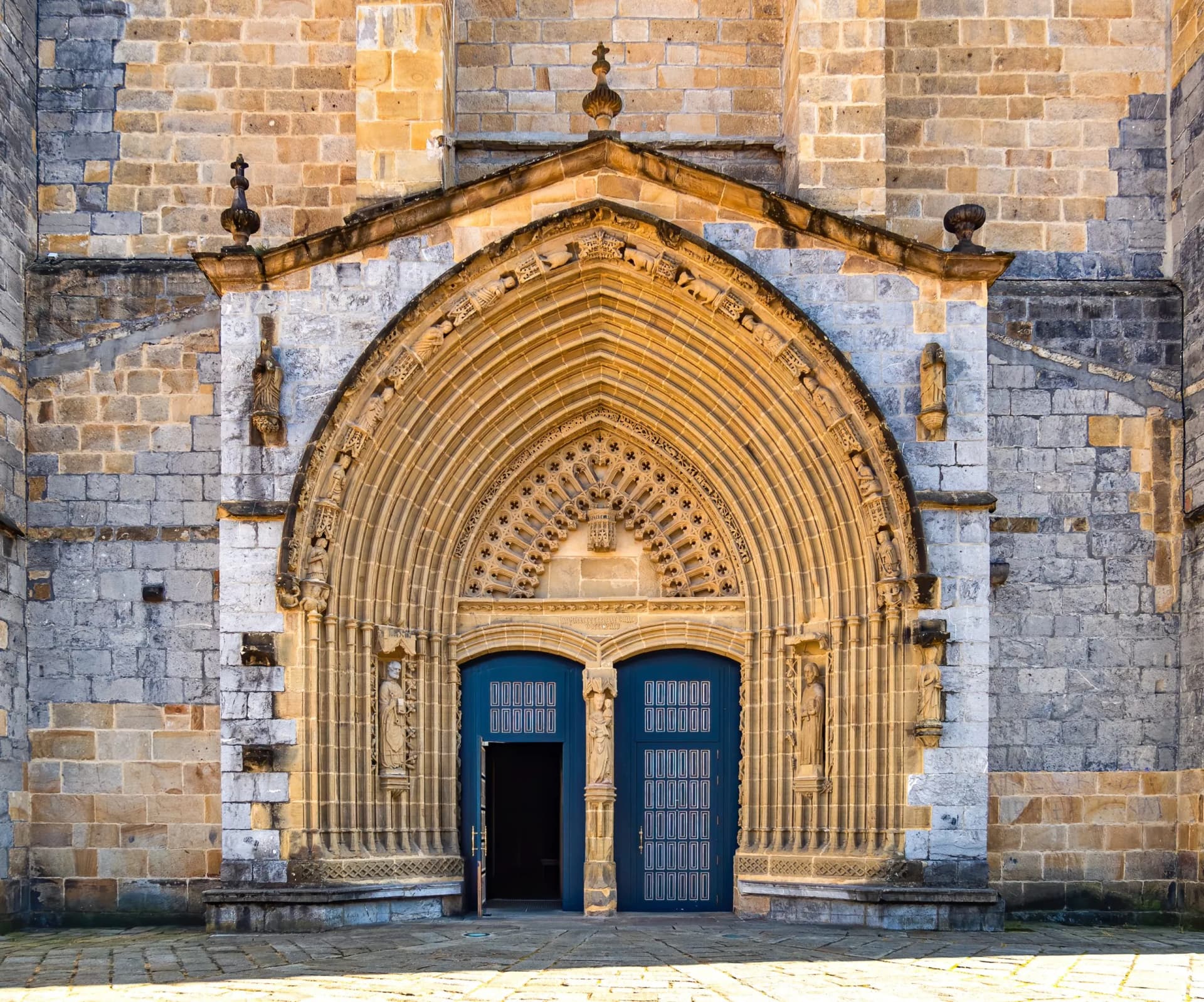 Entrance door and main facade of old stone church in Guernica with ornate stone archway.