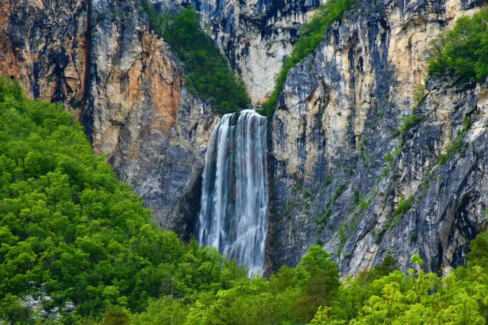 Waterfall cascading down sheer rock cliffs surrounded by vibrant green forest near Bovec.