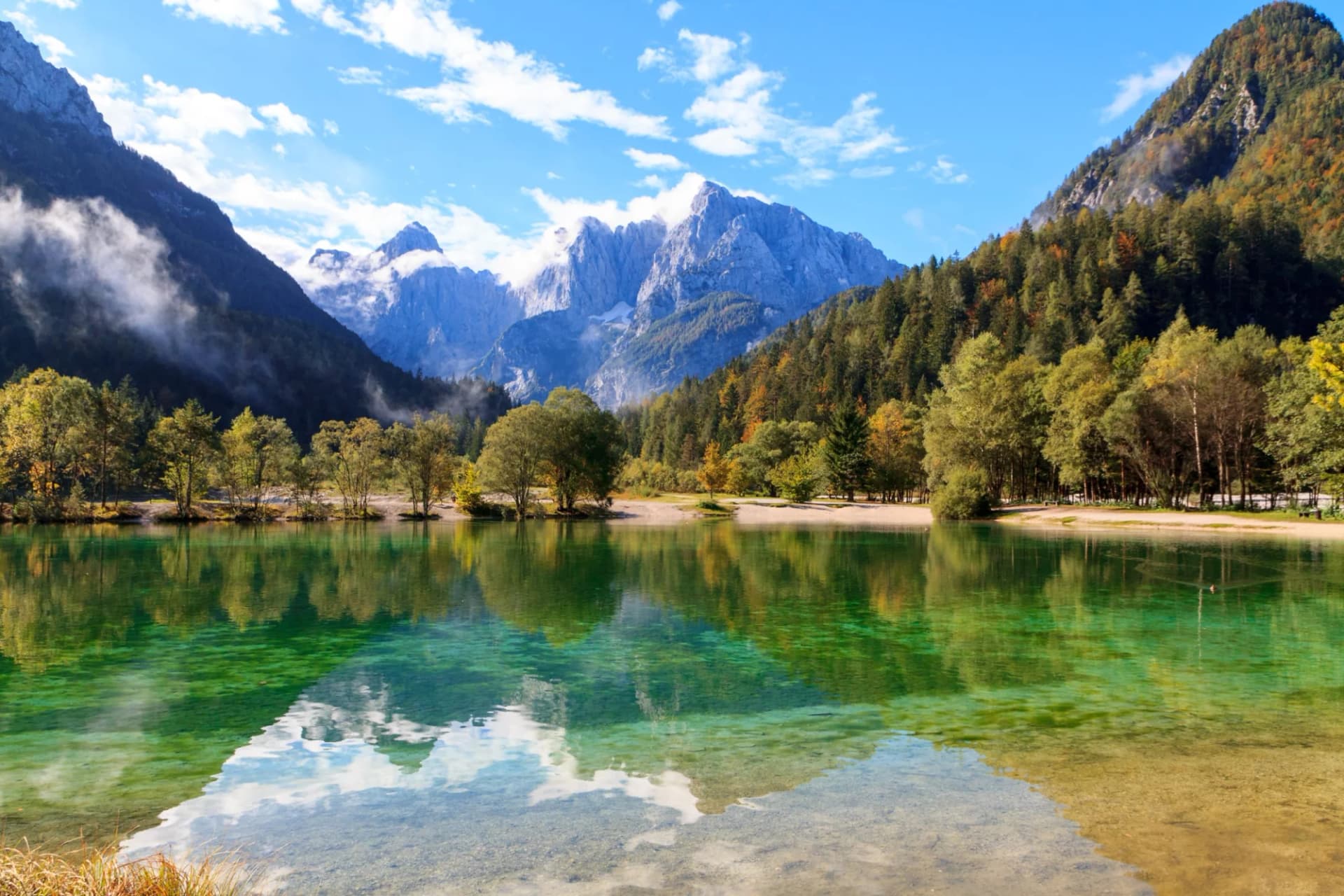 Jasna Lake at Kranjska Gora, Slovenia, with emerald water reflecting jagged mountains and autumn trees.