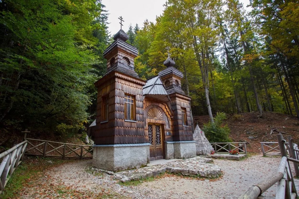 Russian chapel near Vršič Pass with dark wood shingles surrounded by dense forest.