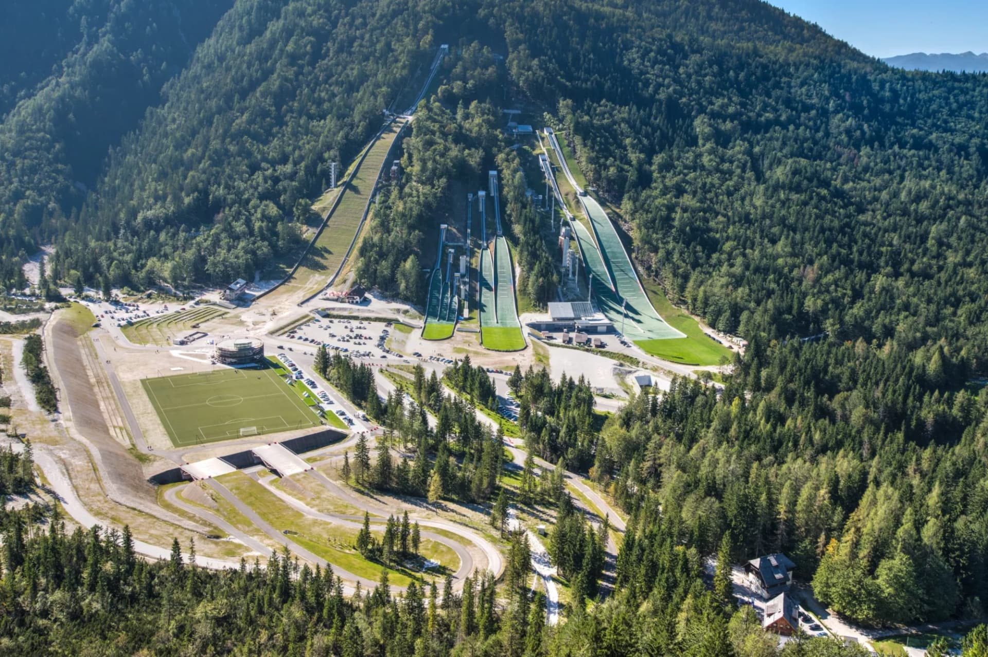 Ski jumping hills and soccer field nestled in a dense evergreen forest in Planica.