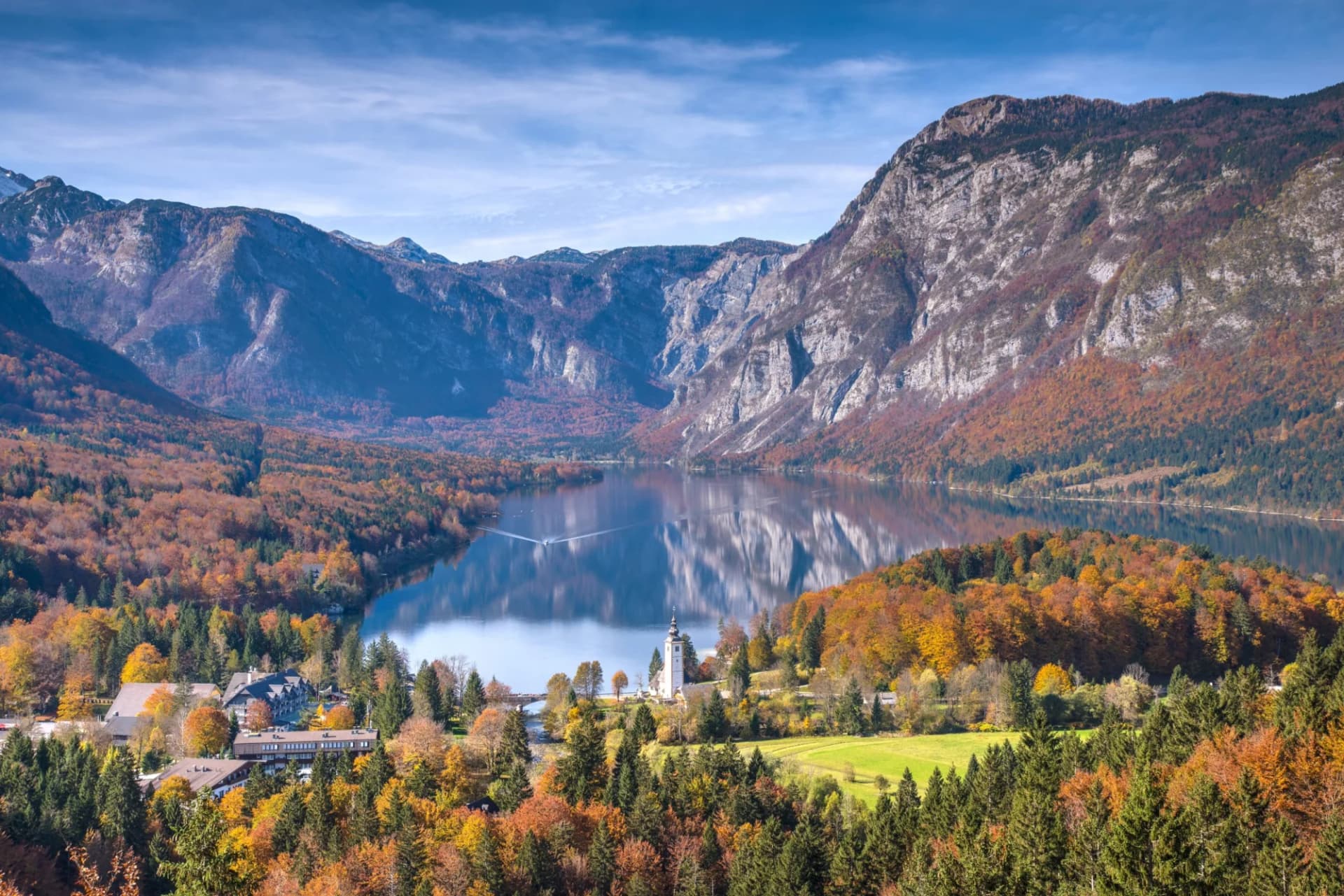 Lake Bohinj with autumn foliage, mountains, and a church reflecting in the calm water.