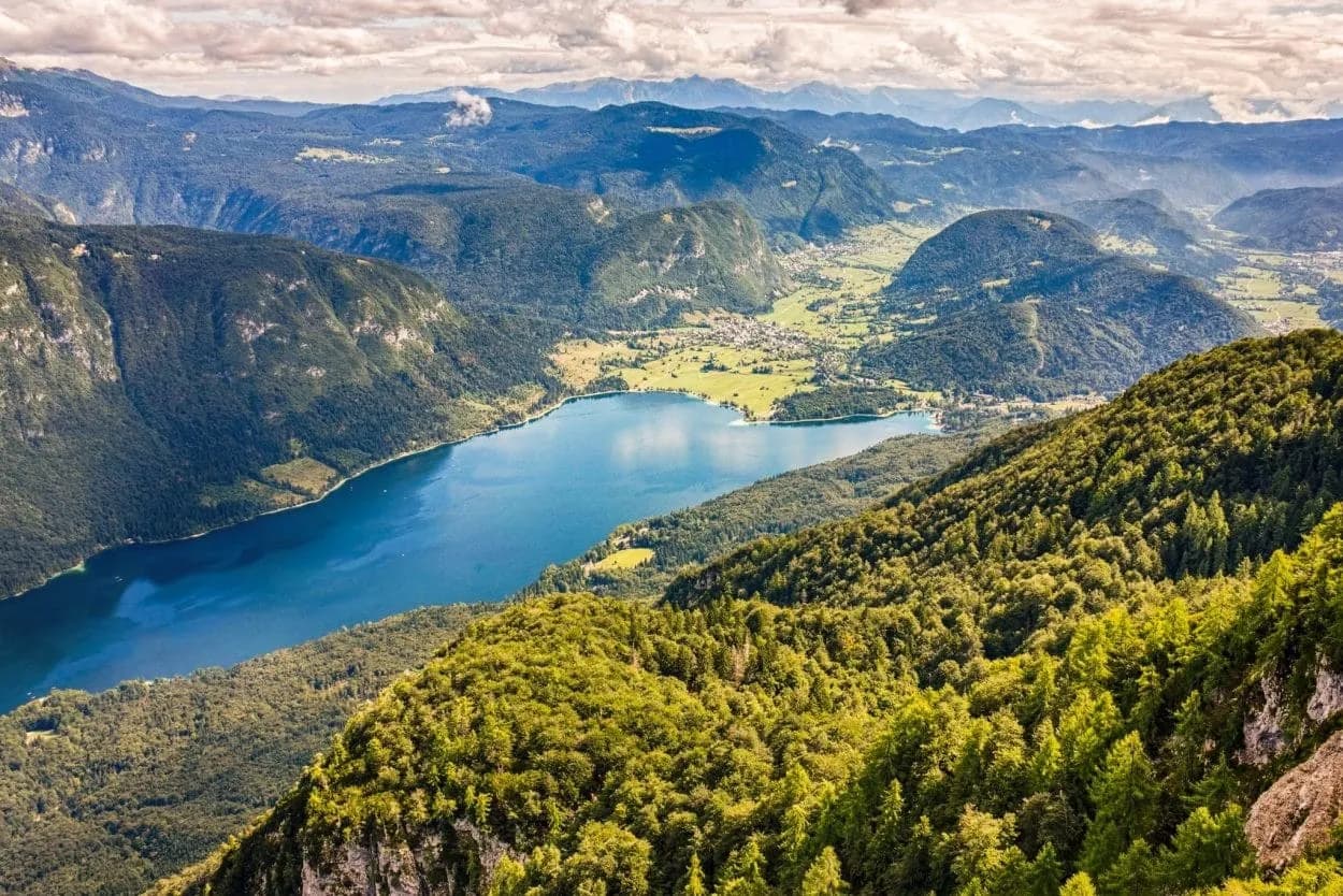 Panoramic view of Bohinj Lake from Vogel mountain with green slopes and distant alpine villages.