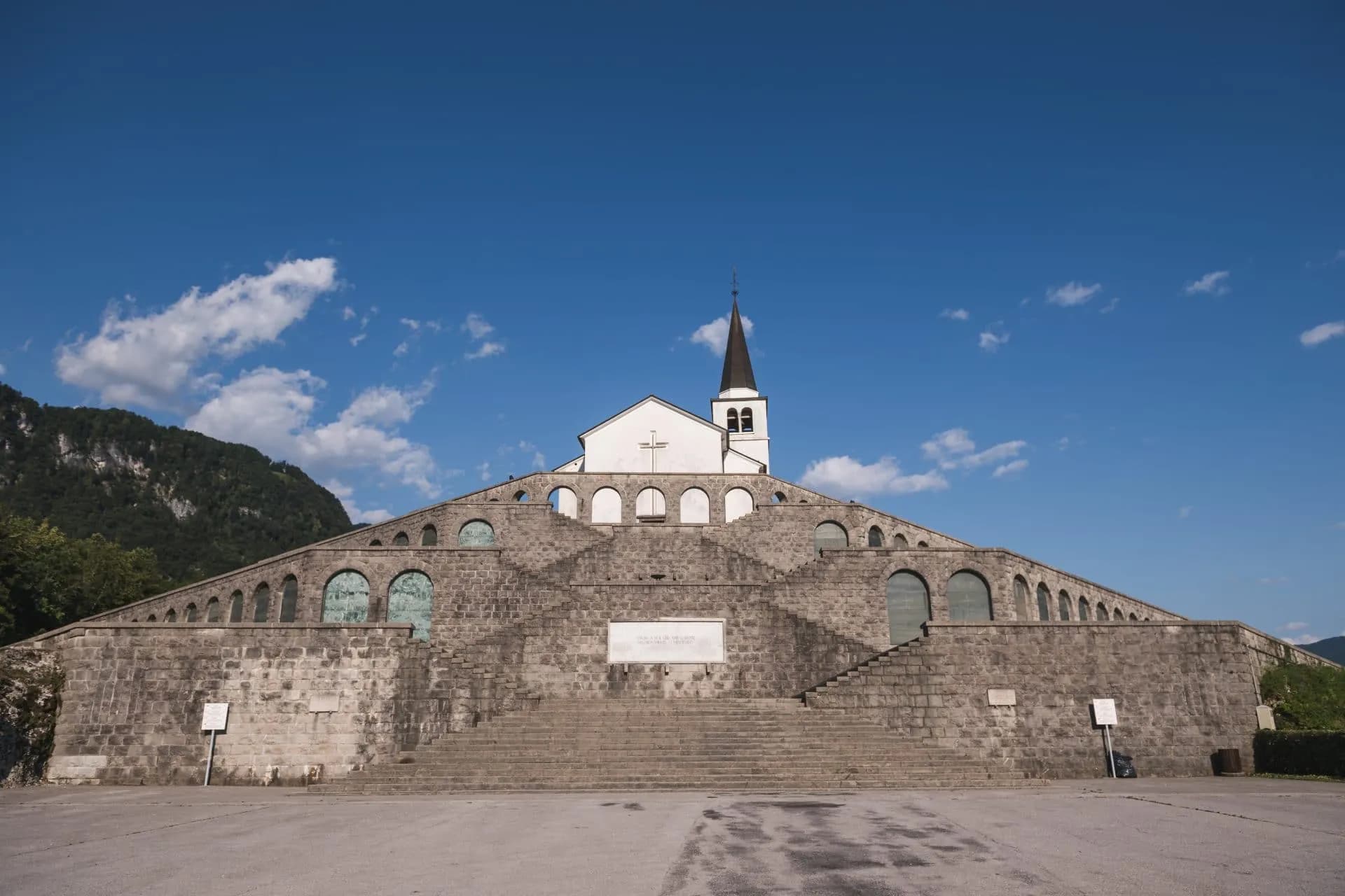 Kobarid Italian Ossuary WWI memorial with steep stone steps and white church under blue sky.