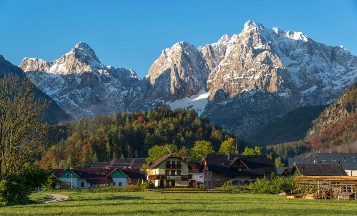 Kranjska Gora village at sunrise with snow-capped Julian Alps and green fields.