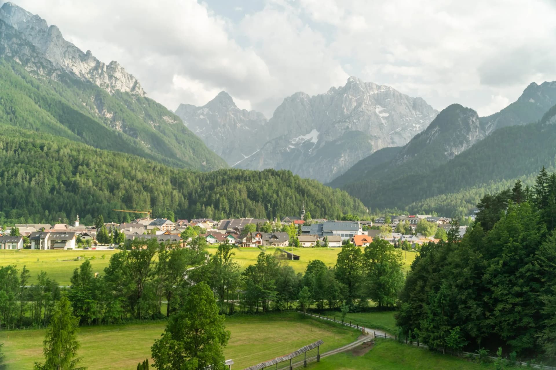 Alpine town nestled in a valley with green fields and snow-capped mountains near Kranjska Gora, Slovenia.