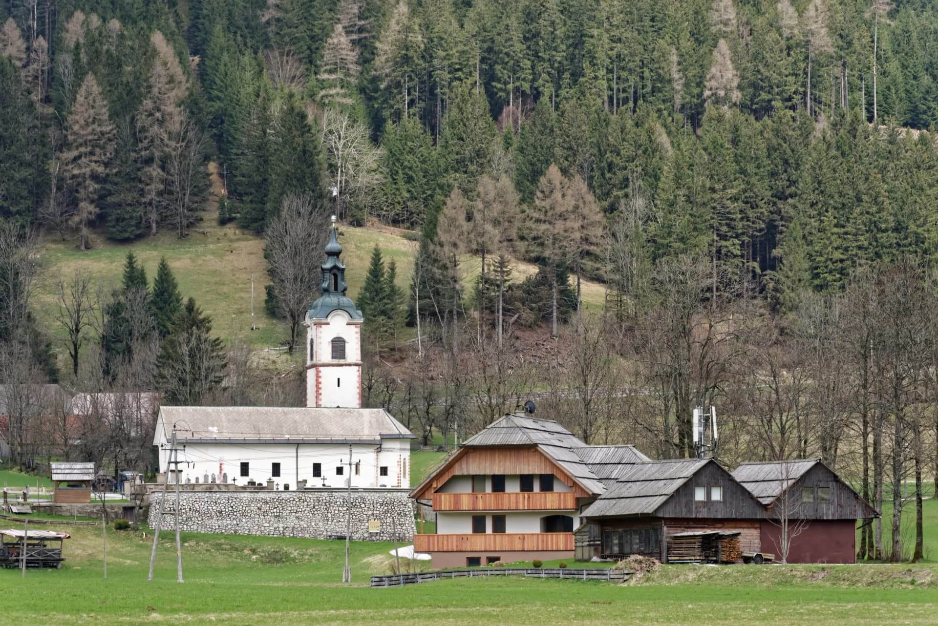 Church with a green spire and white walls next to wooden houses in Zgornje Jezersko valley.