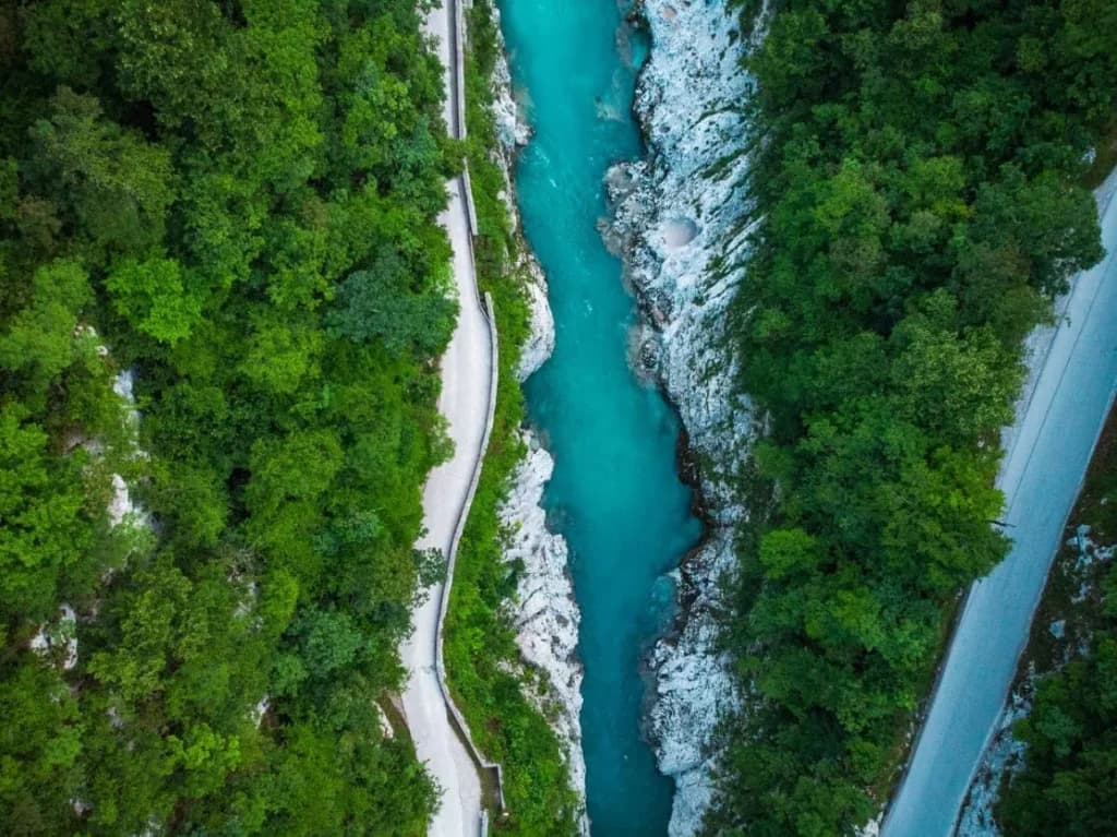 Aerial view of turquoise Soča River canyon with roads and dense green forest
