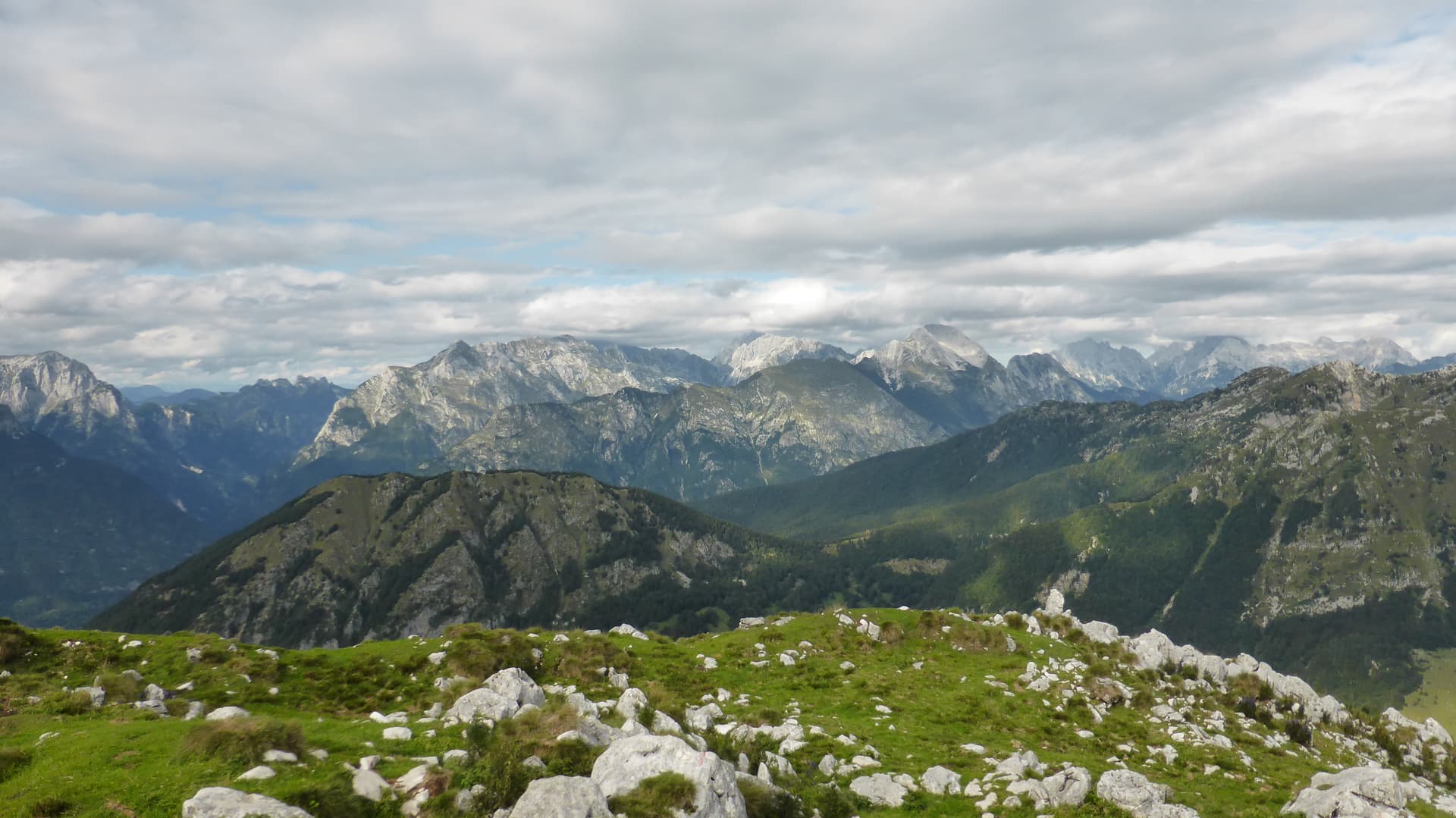 Mountain views from Vršič Pass road with grassy foreground and cloudy sky.
