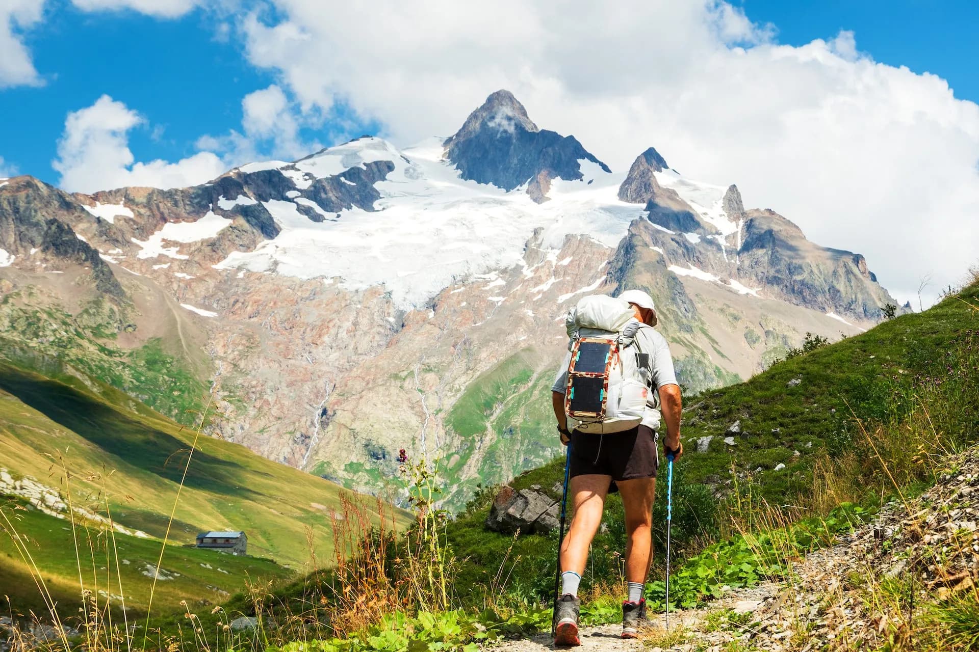Hiker with backpack and poles ascending trail toward snow-capped Aiguille des Glaciers.