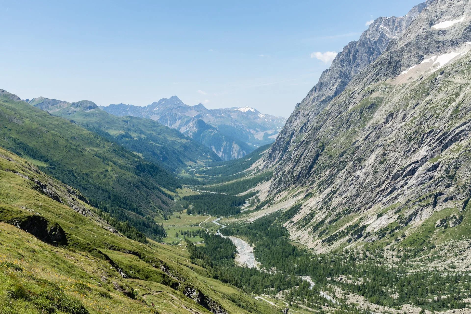 View of Ferret valley at Aosta with steep green slopes, rocky mountains, and a winding river.