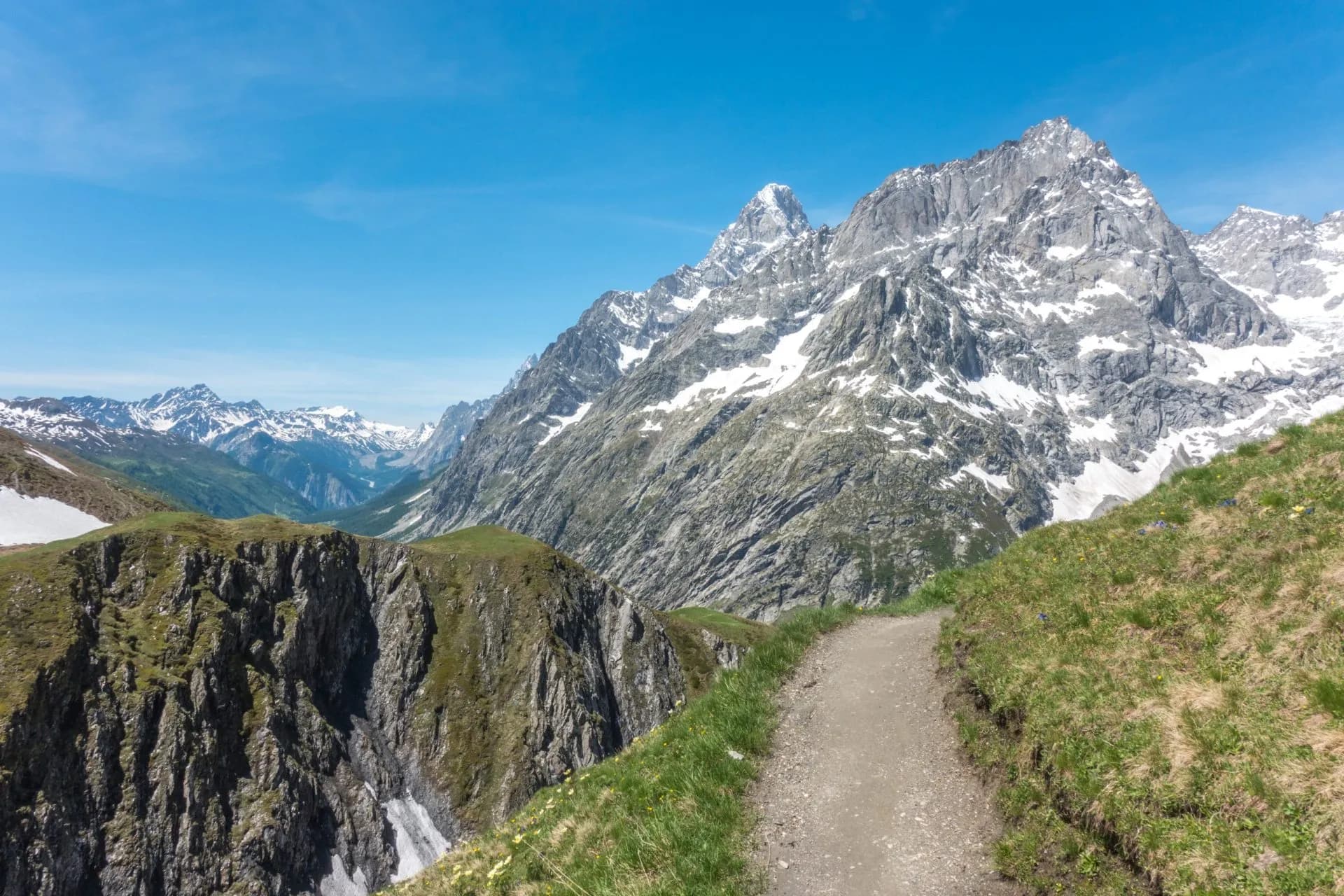 Hiking trail along grassy ridge toward snow-capped mountains at Col du Ferret.