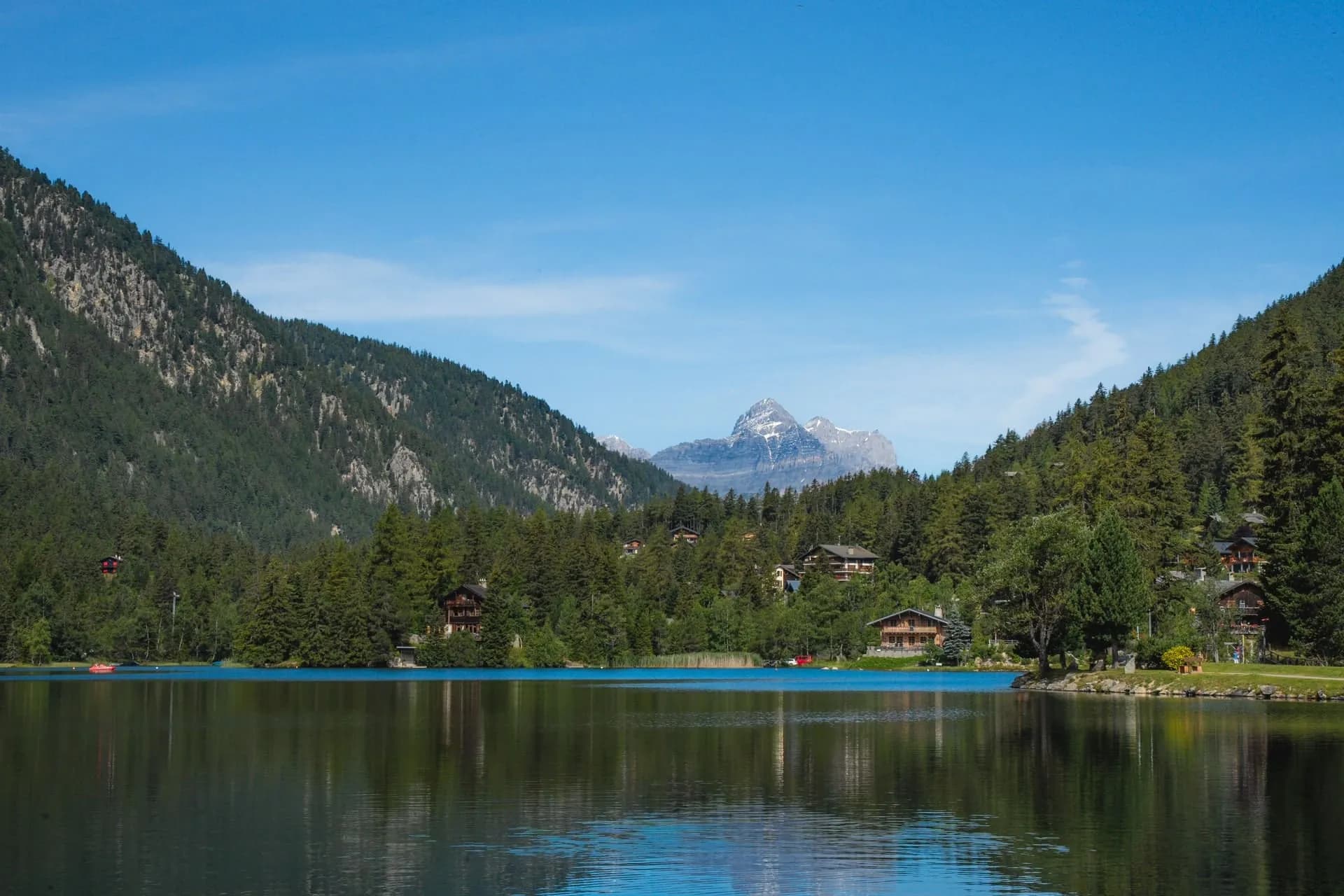 Calm lake reflecting mountains and lakeside chalets in Champex-Lac under a clear blue sky.